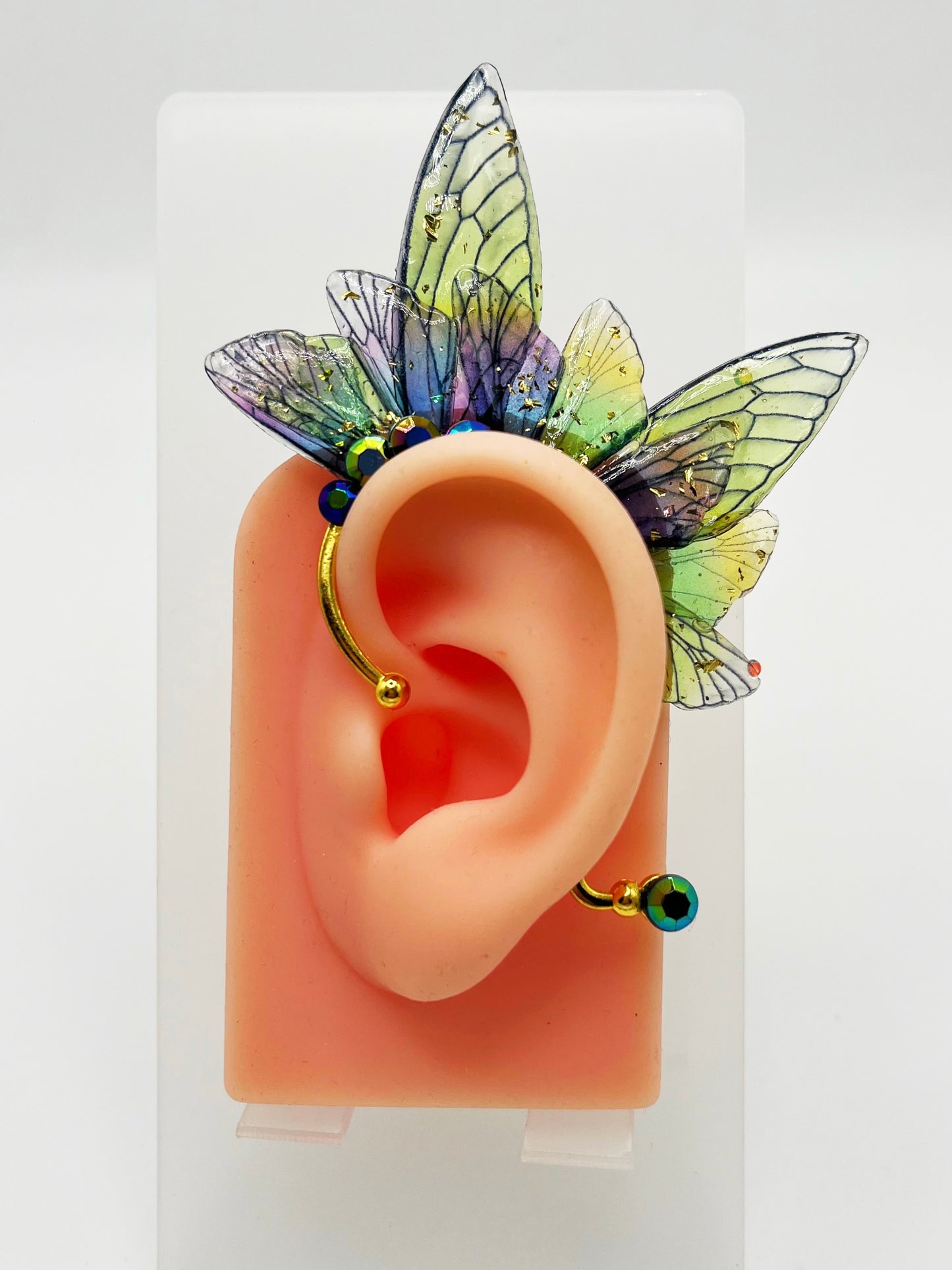 Green and purple fairy wing ear cuff with blue rhinestones, modeled on an ear.