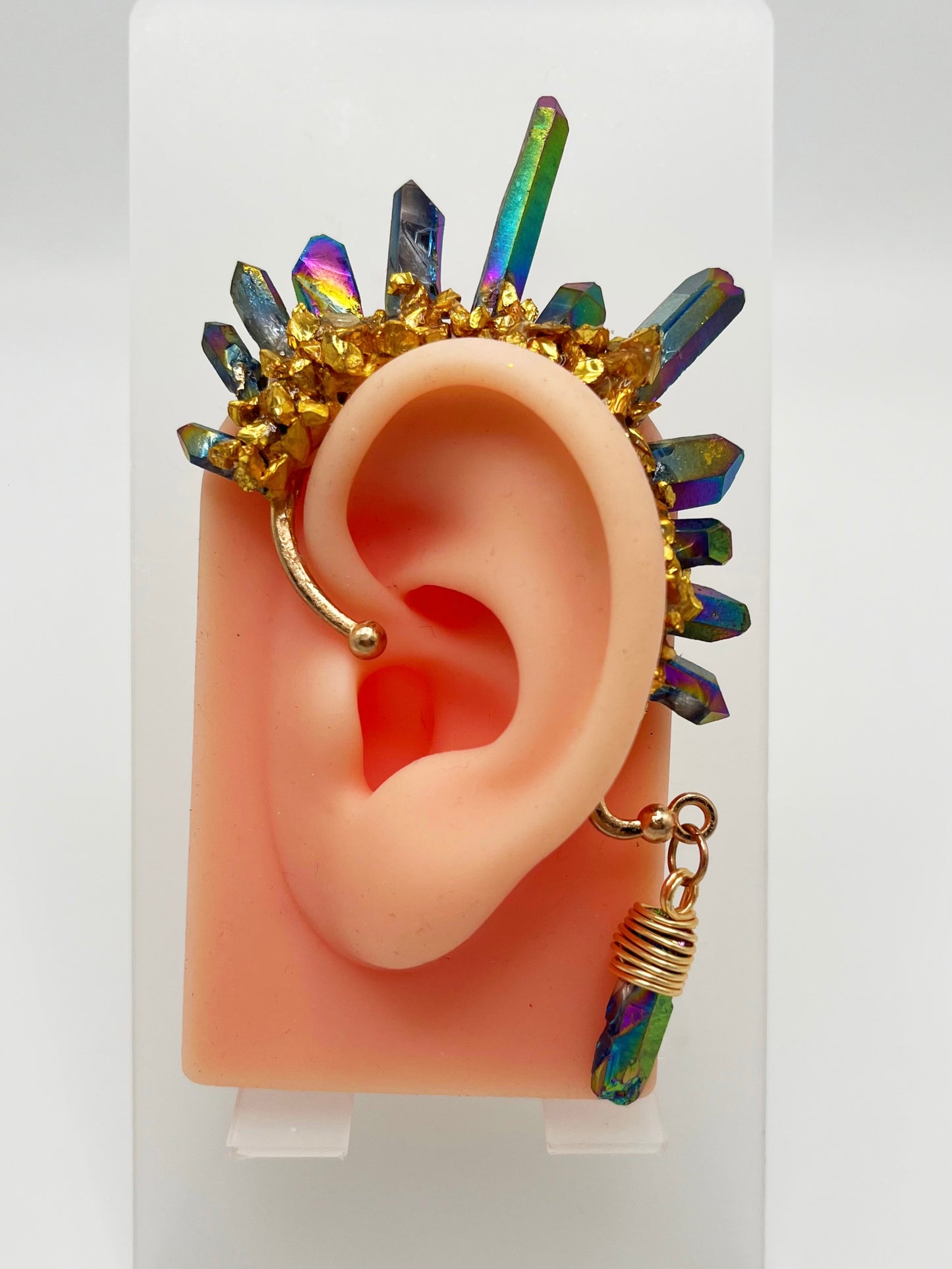 Blue rainbow titanium quartz crystal ear cuff with gold accents, modeled on an ear. A wire wrapped stone hangs from the bottom of the cuff behind the ear.