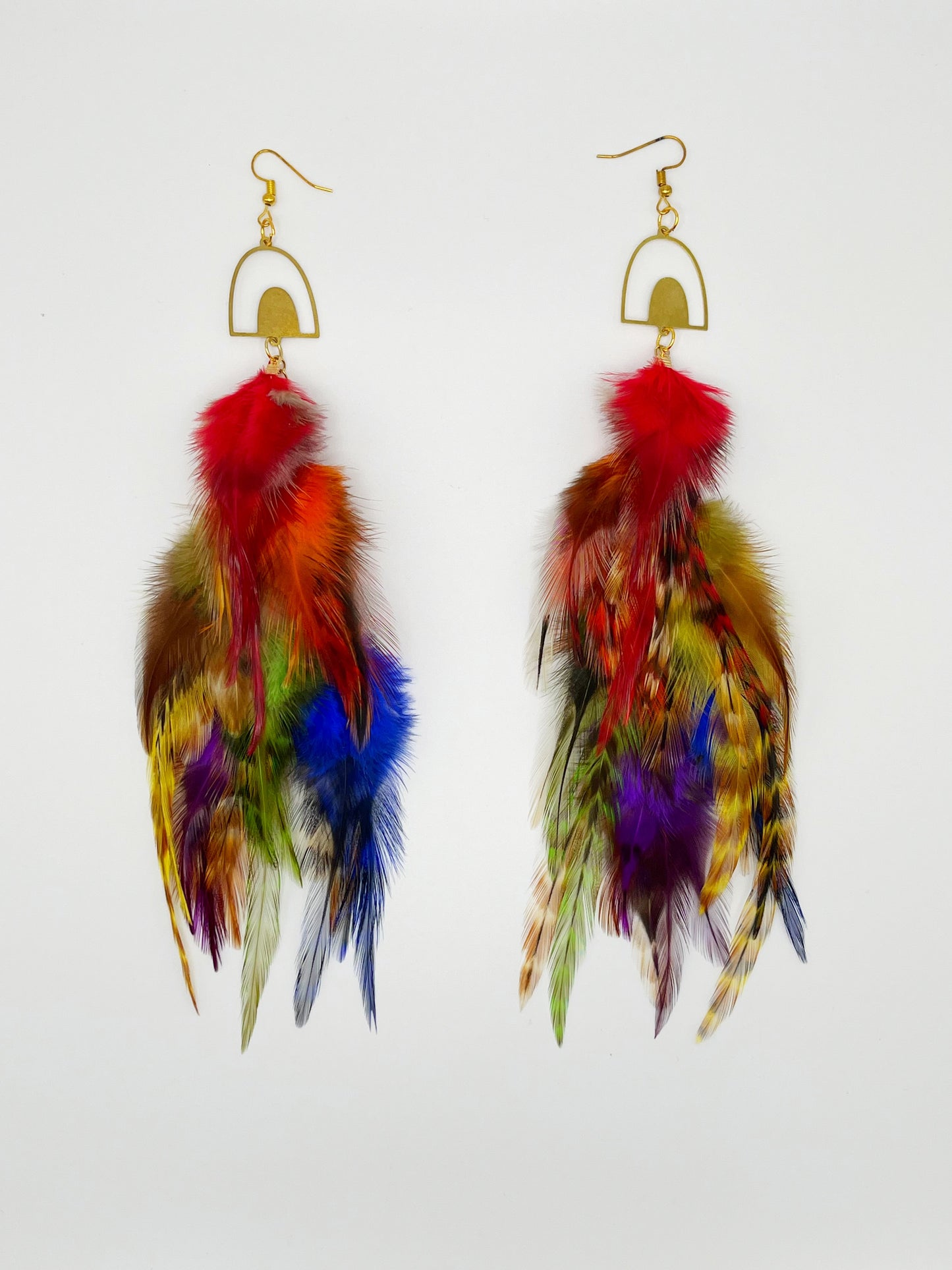 Long bohemian feather earrings in rainbow colors, hanging from a gold rainbow pendant.