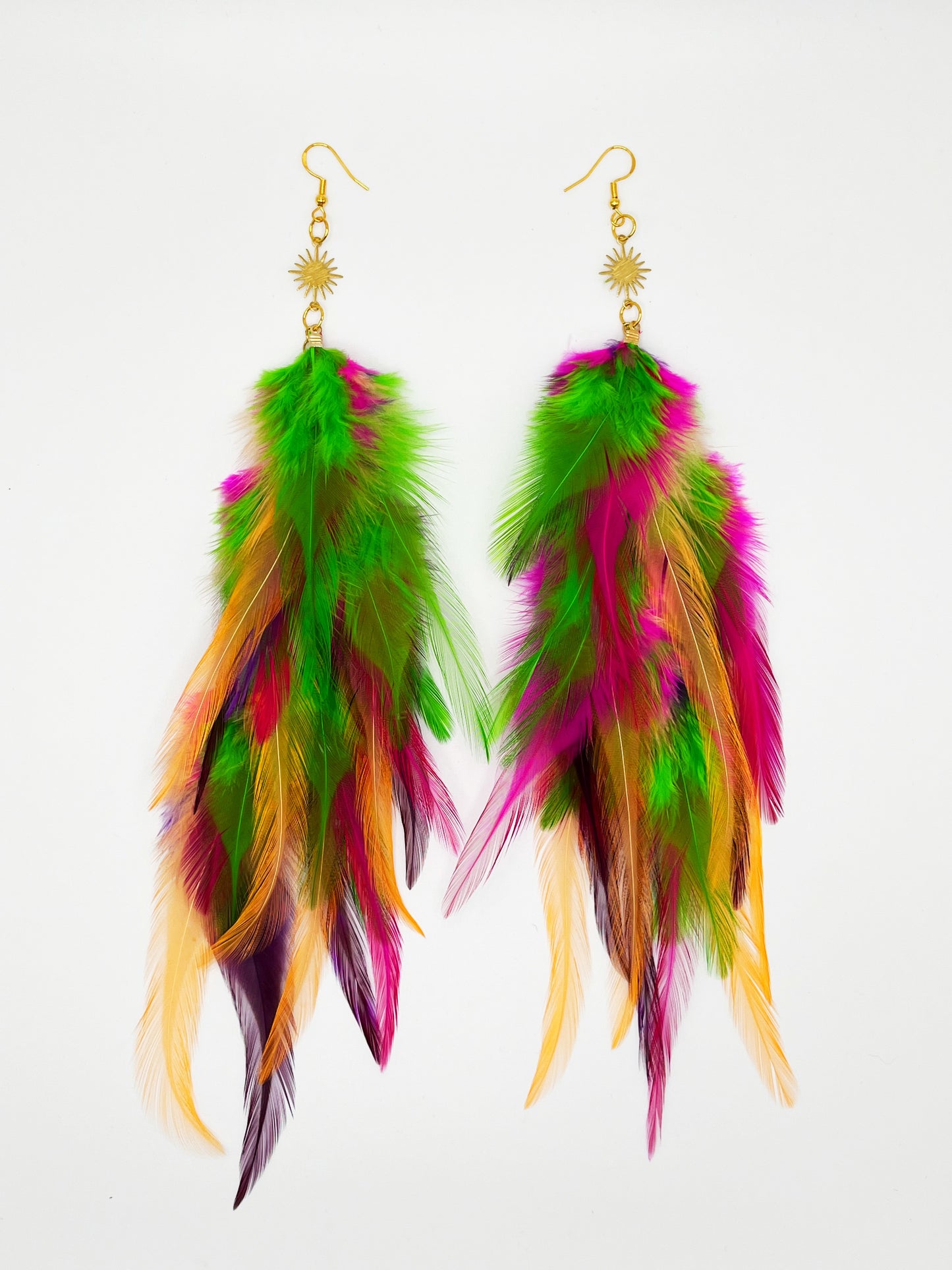 Long bohemian feather earrings in bright green, pink, purple and orange tones, hanging from a gold sun pendant.