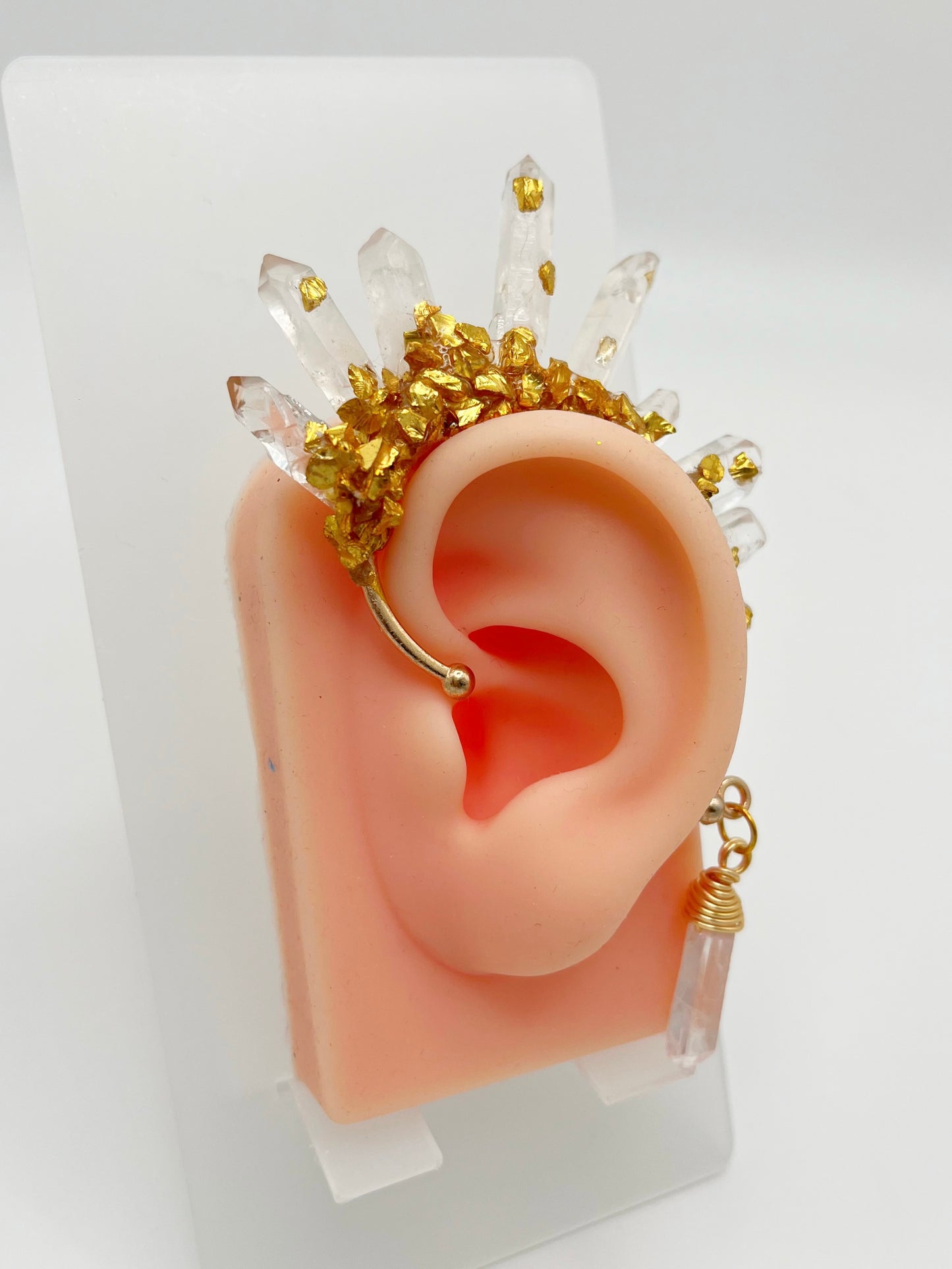 Clear quartz crystal ear cuff with crushed gold accents, modelled on an ear. A wire wrapped quartz stone hangs from the bottom of the cuff behind the ear.