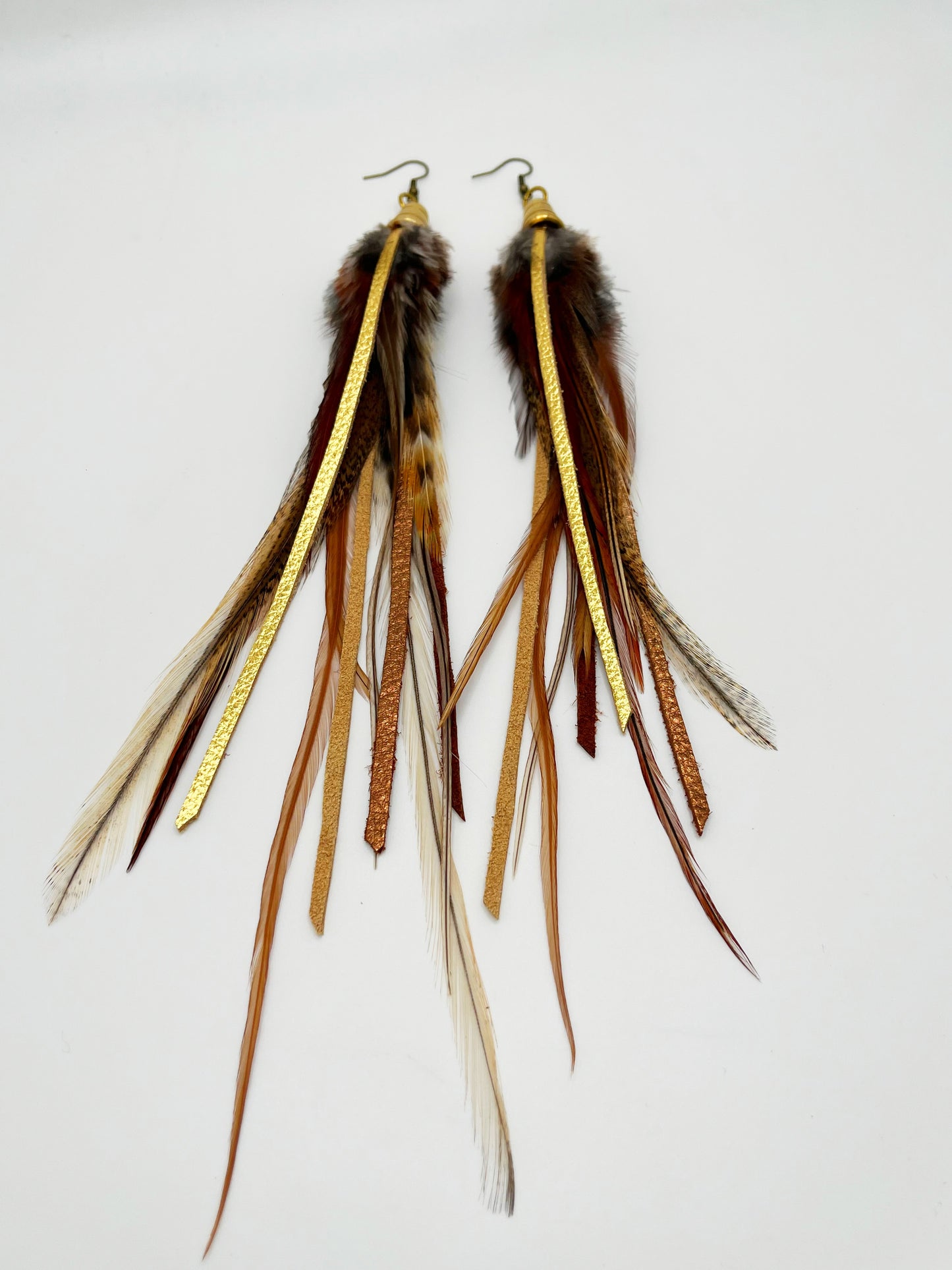Dark brown feather earrings with metallic gold and bronze leather strips, hanging from a gold colored cap pendant.