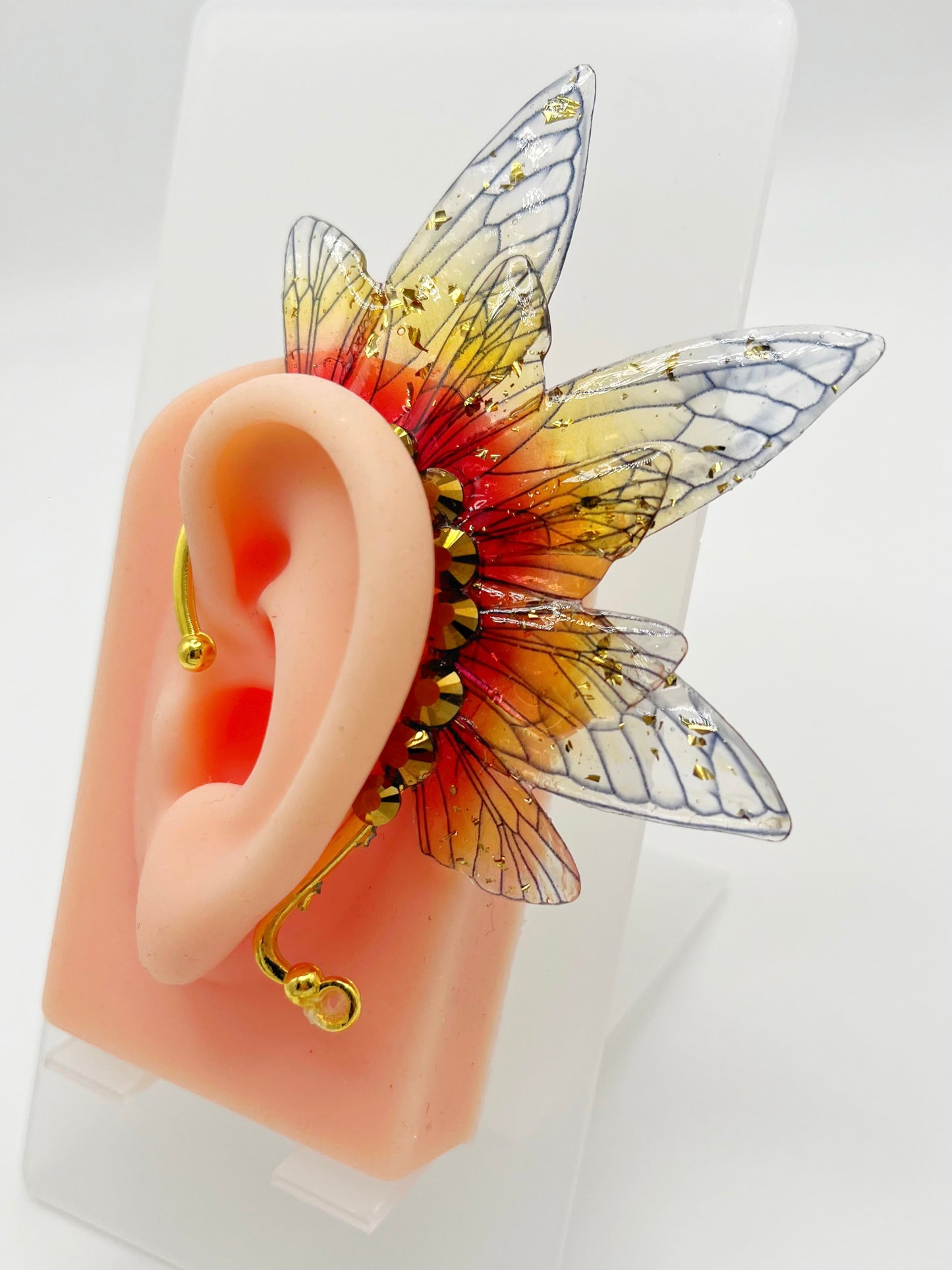 Yellow and red fairy wing ear cuff with gold rhinestones, modeled on an ear.