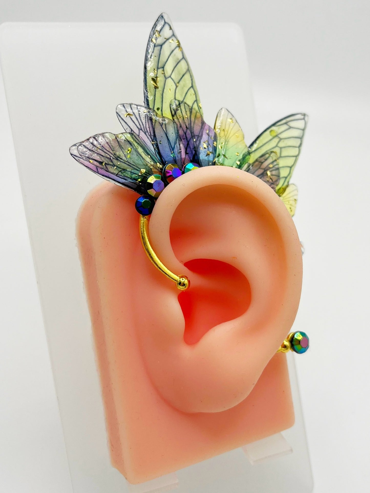 Green and purple fairy wing ear cuff with blue rhinestones, modeled on an ear.