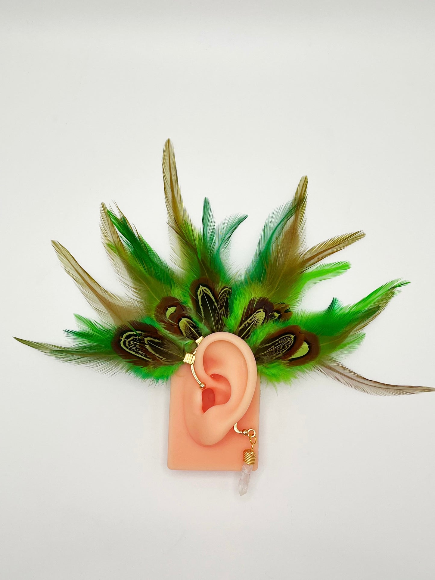 Vibrant green rooster feather ear cuff with brown green pheasant feathers, modeled on an ear. A wire wrapped quartz stone hangs from the cuff behind the ear.