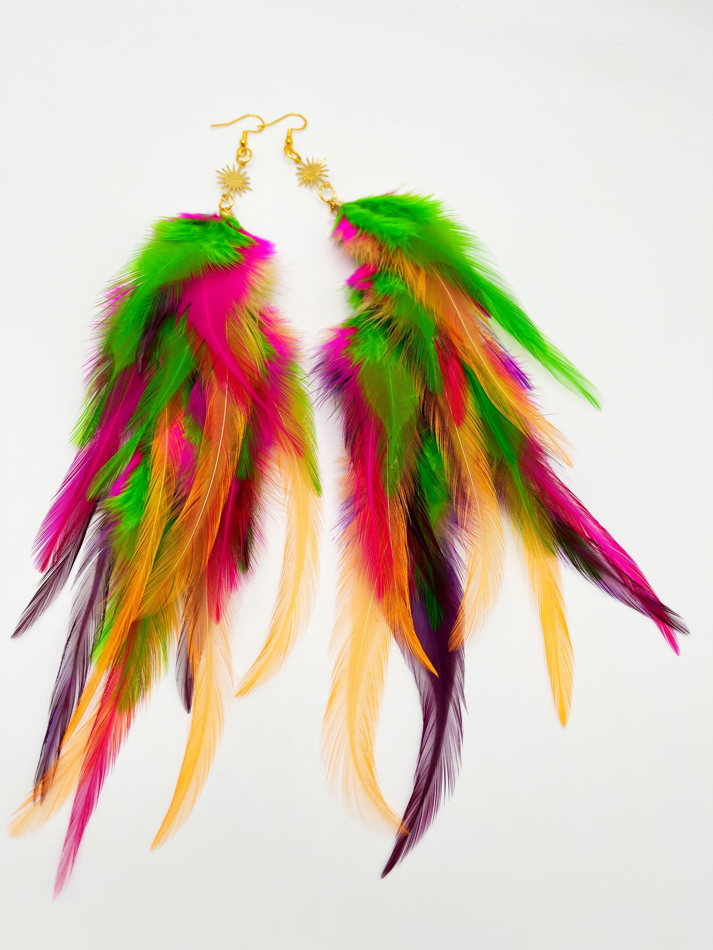 Long bohemian feather earrings in bright green, pink, purple and orange tones, hanging from a gold sun pendant.