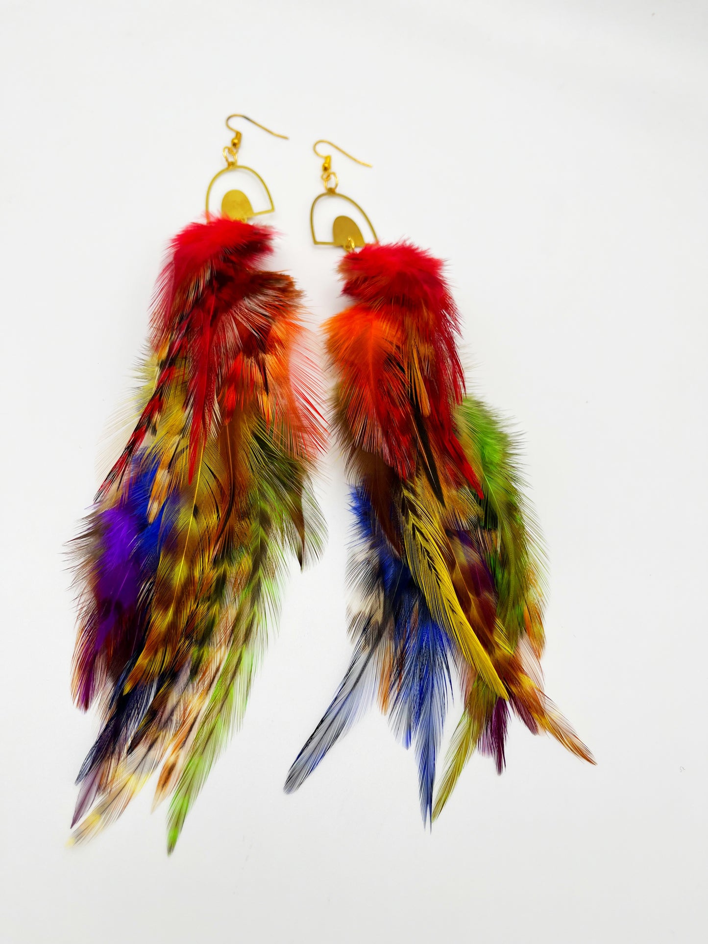 Long bohemian feather earrings in rainbow colors, hanging from a gold rainbow pendant.