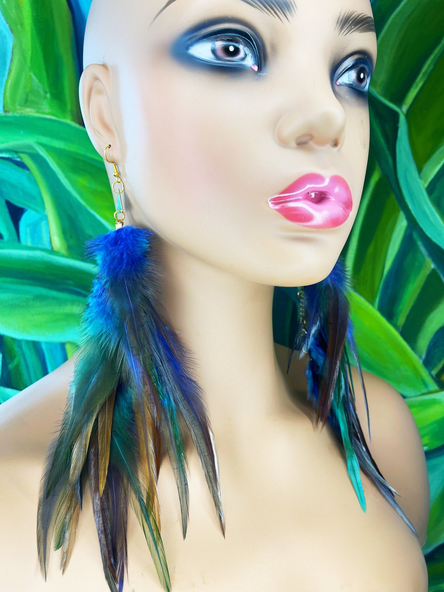 Long bohemian feather earrings in blue, gray and turquoise tones, modeled on a mannequin head.