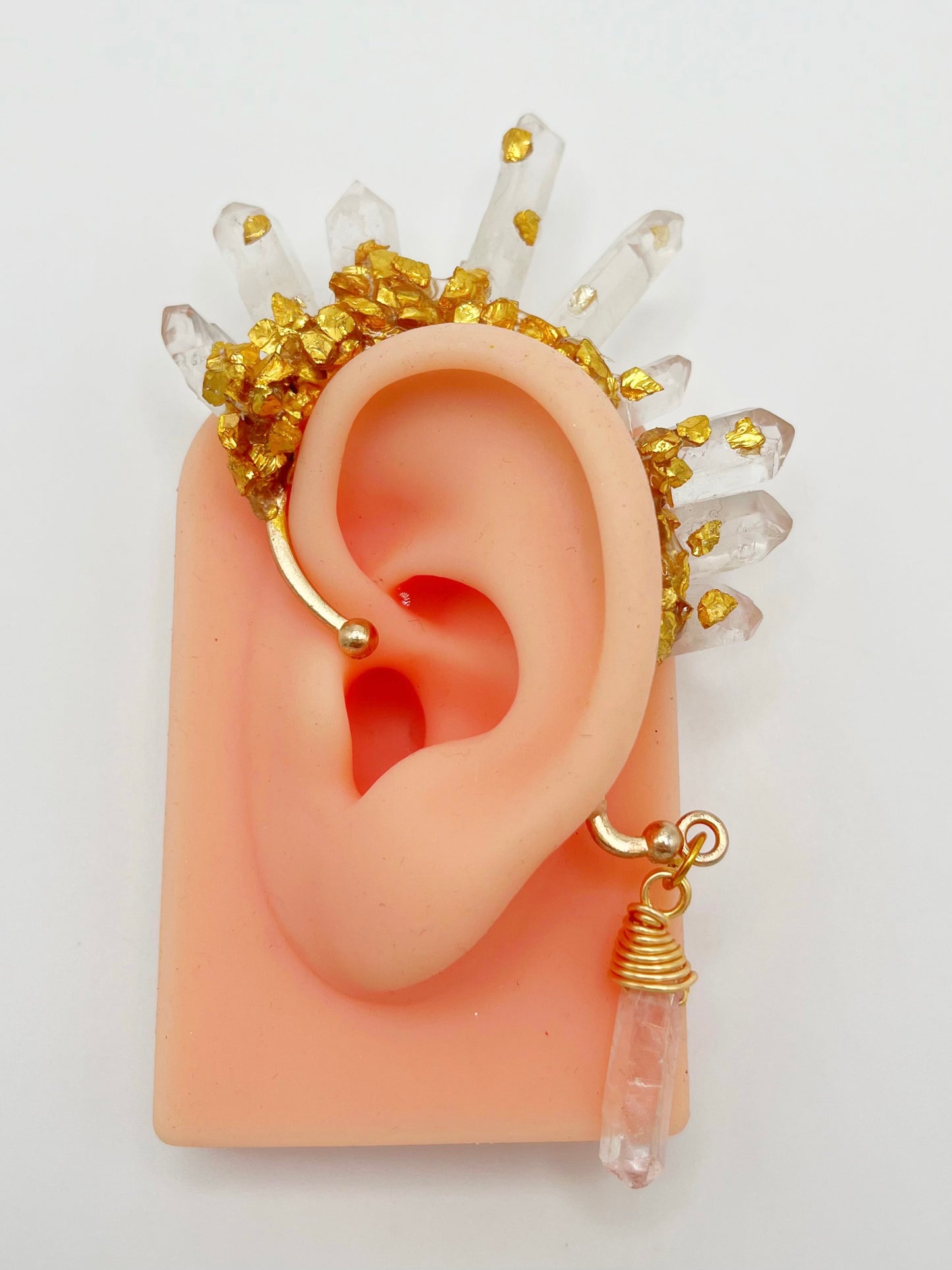 Clear quartz crystal ear cuff with crushed gold accents, modelled on an ear. A wire wrapped quartz stone hangs from the bottom of the cuff behind the ear.