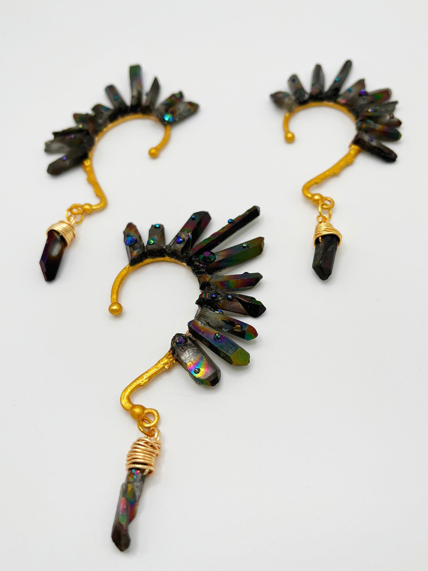 Black rainbow quartz crystal ear cuffs with blue rhinestones. A wire wrapped stone hangs from the bottom of each cuff.