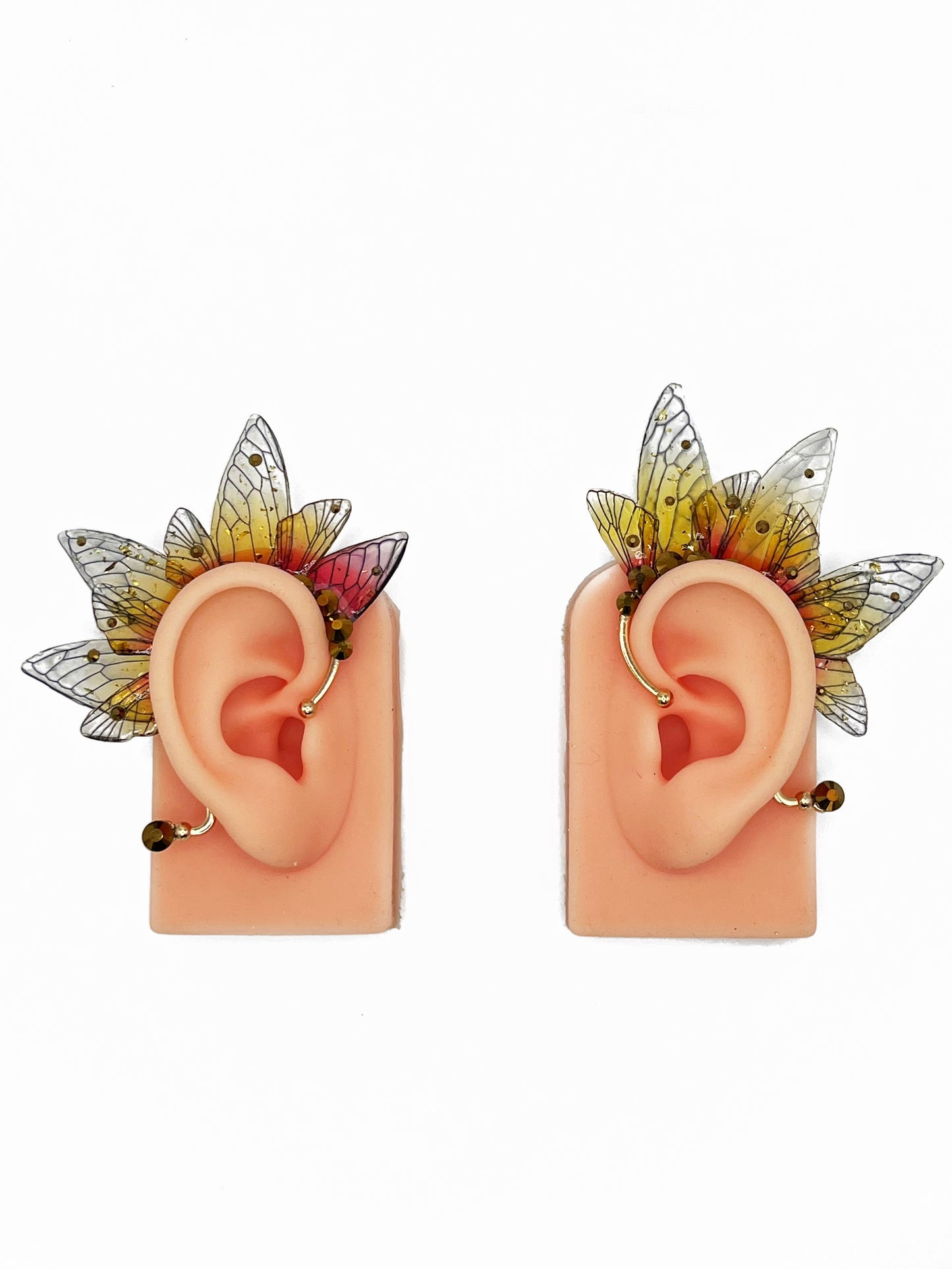Yellow and red fairy wing ear cuffs with gold rhinestones, modeled on a pair of ears.