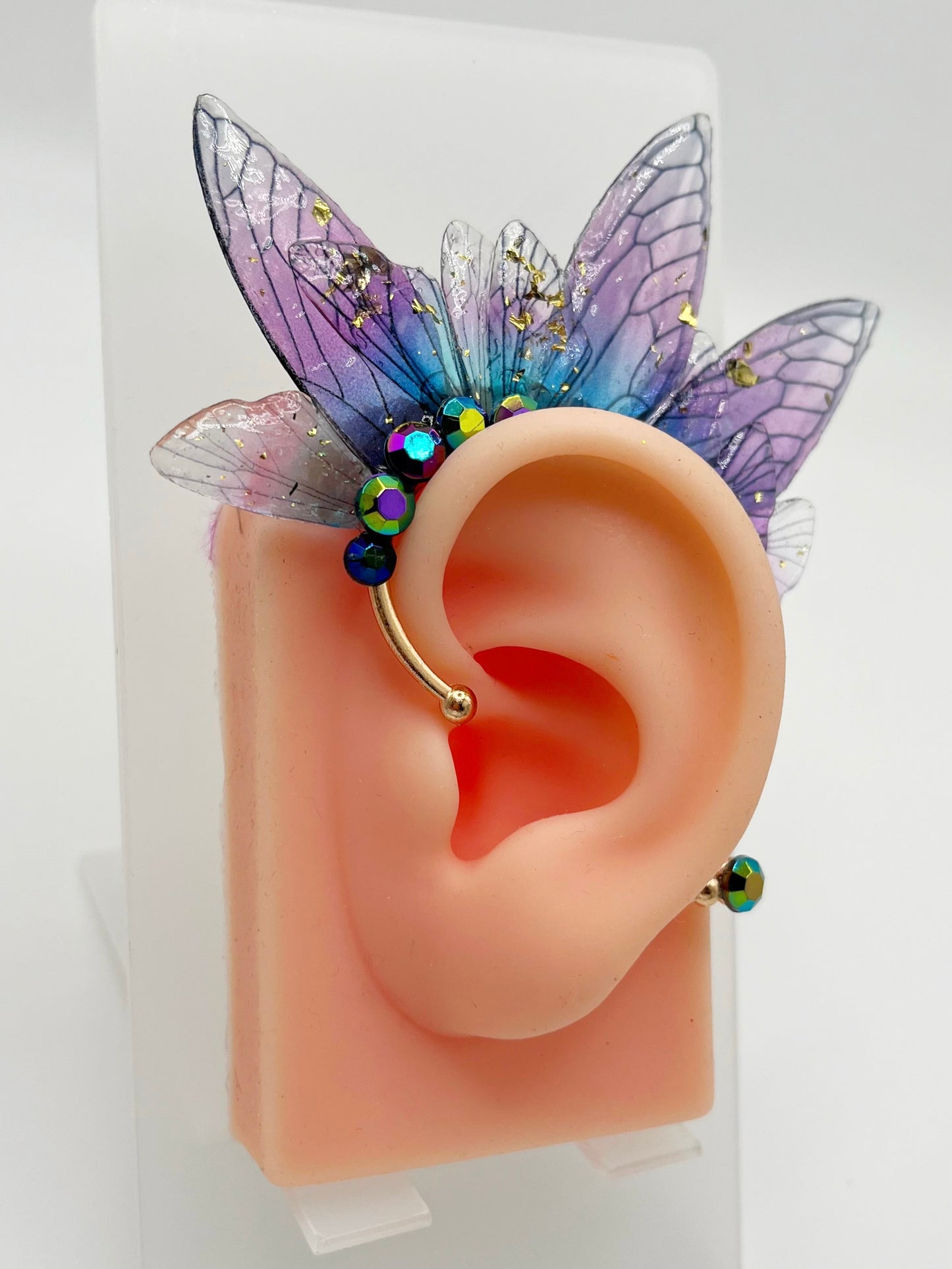 Purple fairy wing ear cuff with blue rhinestones, modeled on an ear.