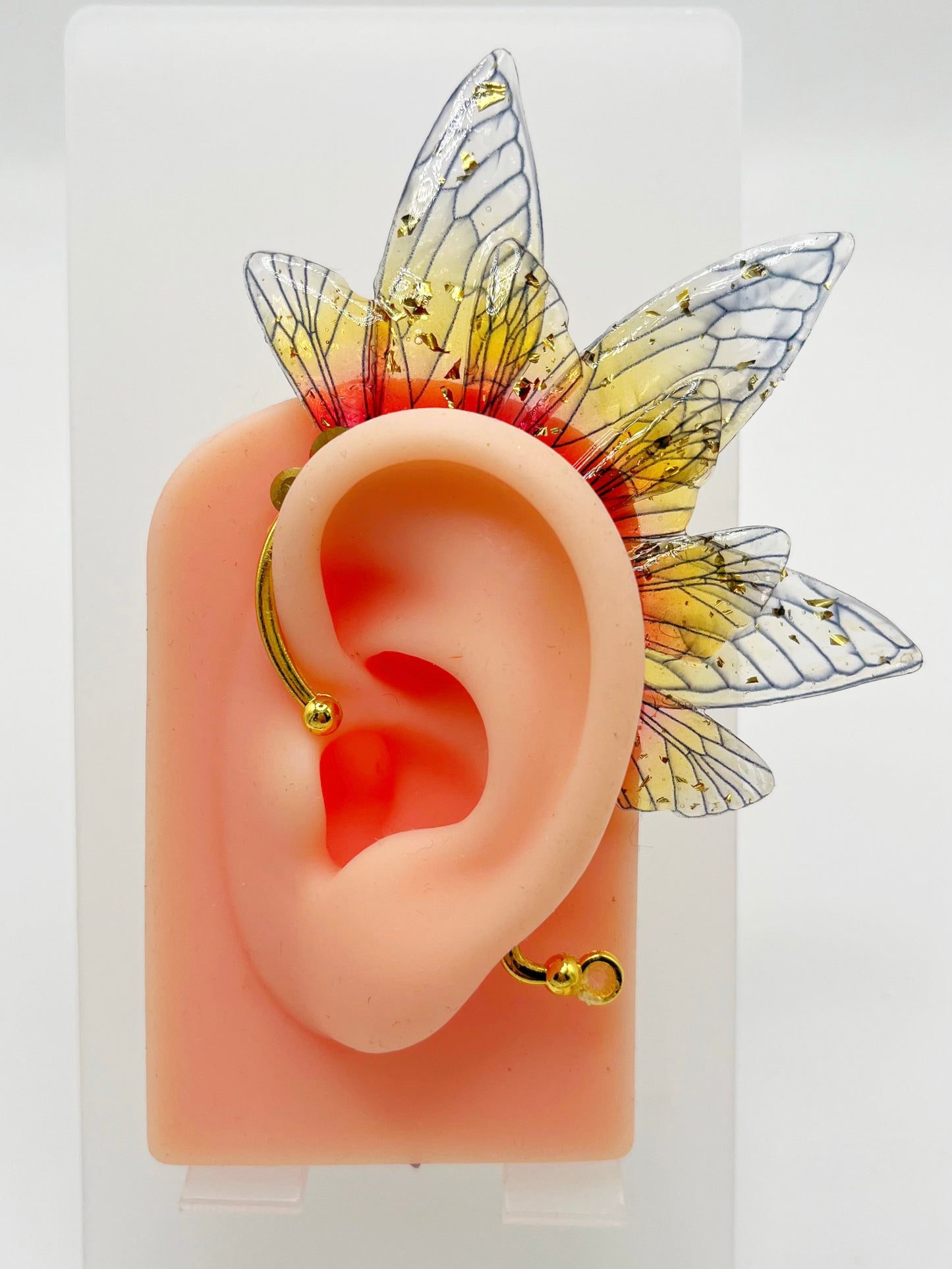 Yellow and red fairy wing ear cuff with gold rhinestones, modeled on an ear.