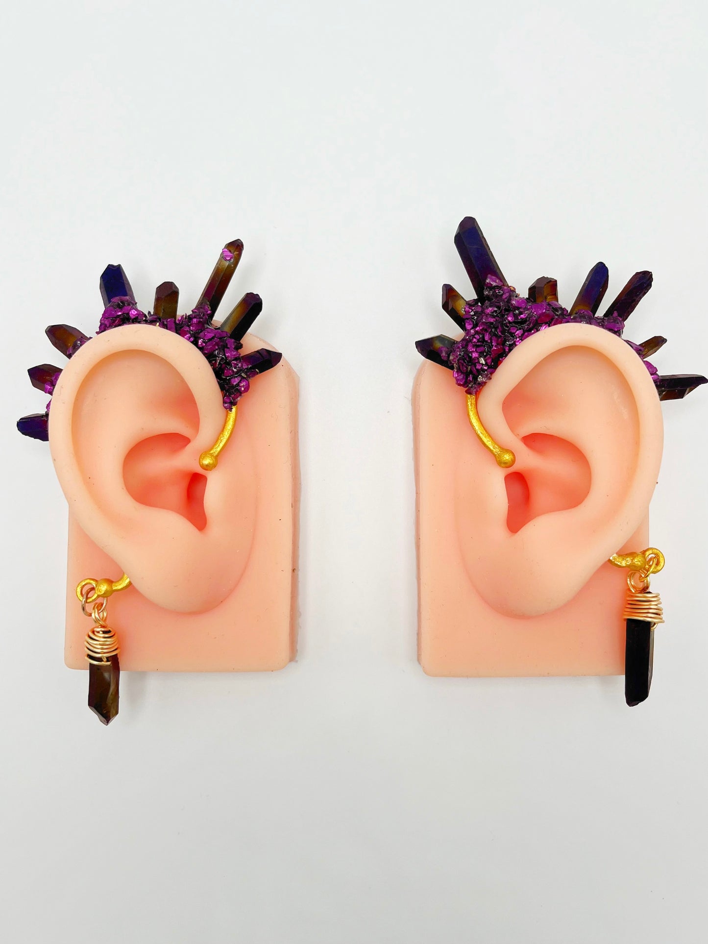 Purple titanium quartz ear cuffs with purple metallic accents, modeled on a pair of ears. A wire wrapped quartz is attached to the bottom of each cuff that hangs behind the ear.