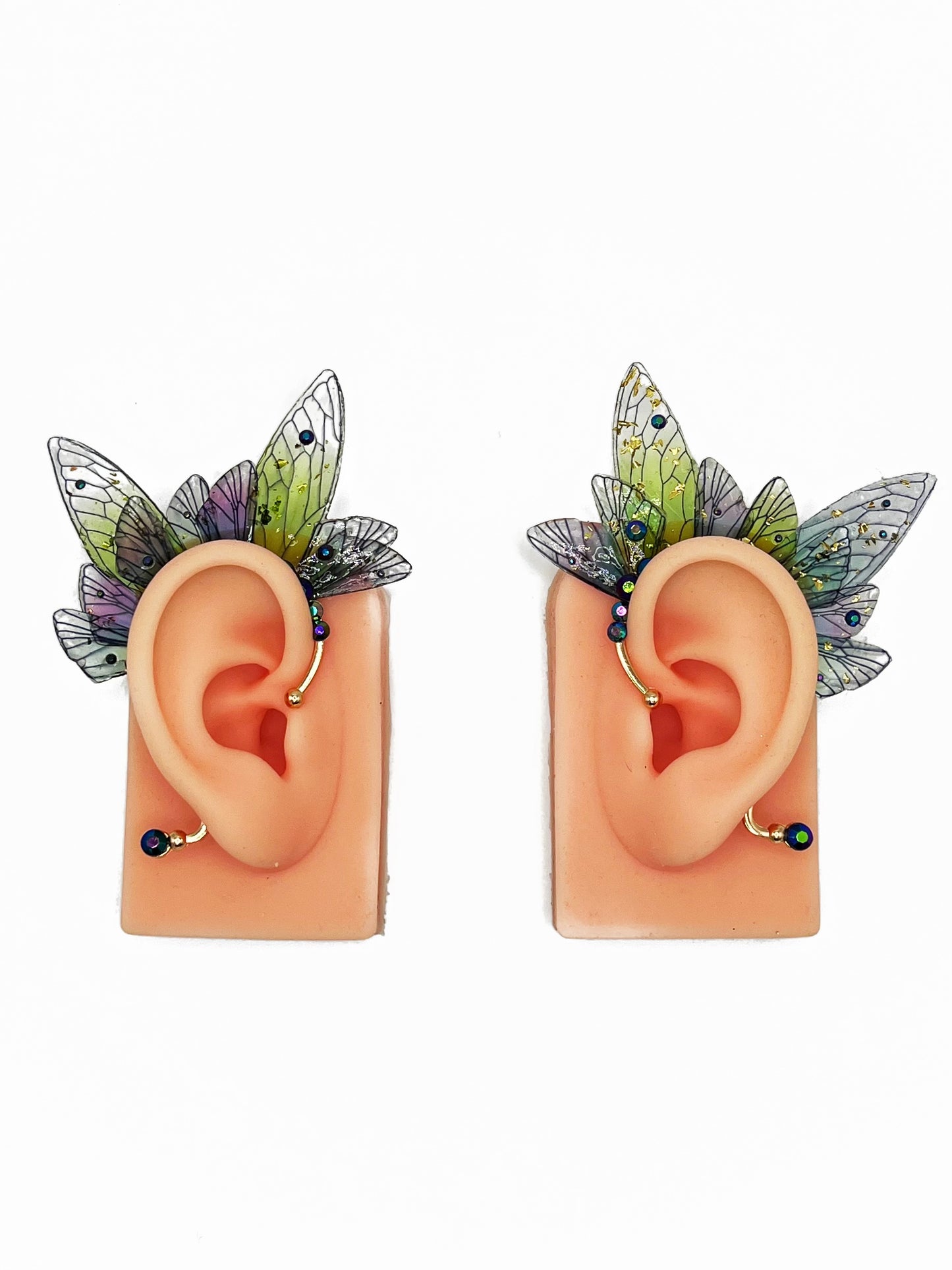 Green and purple fairy wing ear cuffs with blue rhinestones, modeled on a pair of ears.