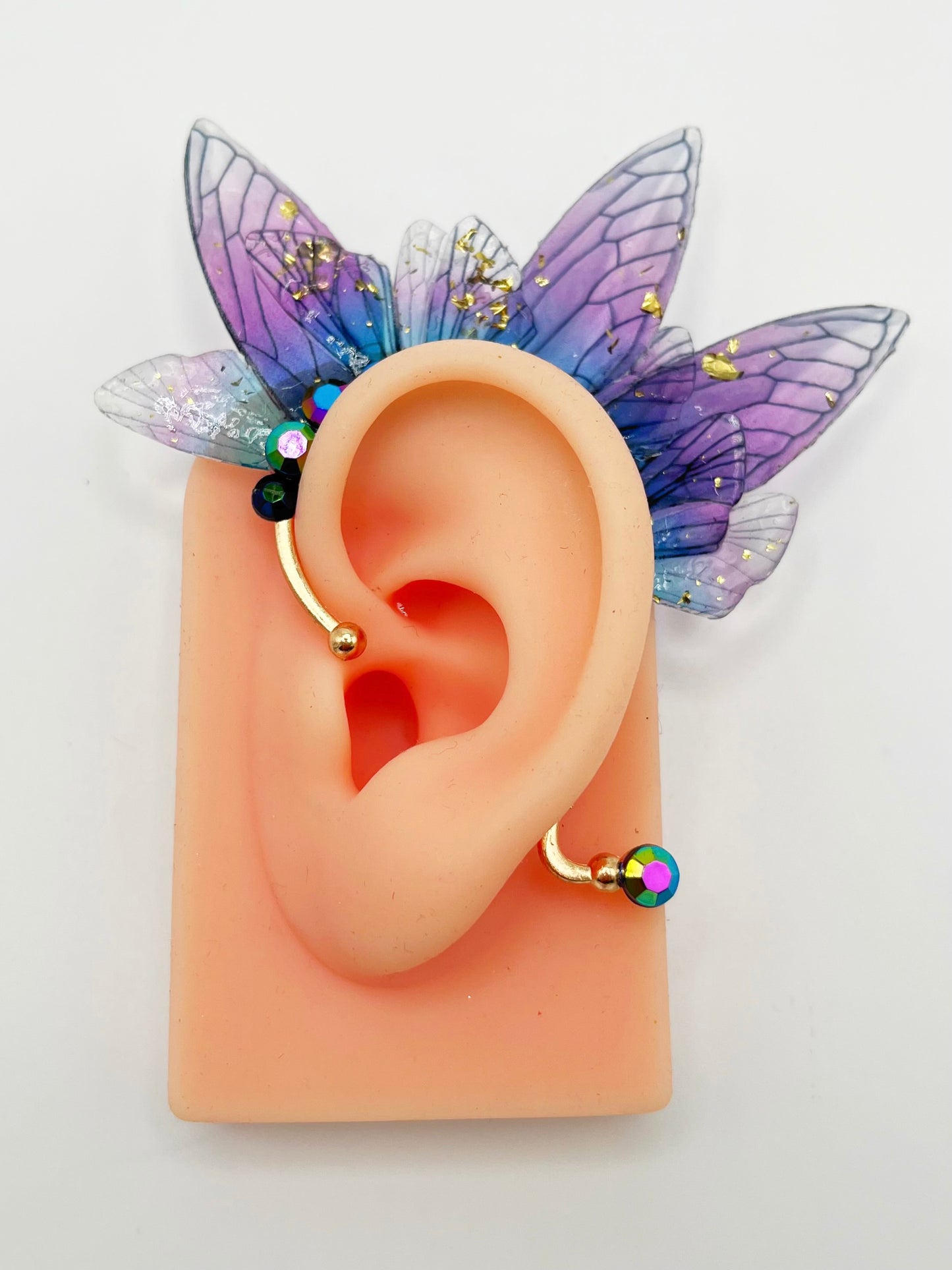 Purple fairy wing ear cuff with blue rhinestones, modeled on an ear.