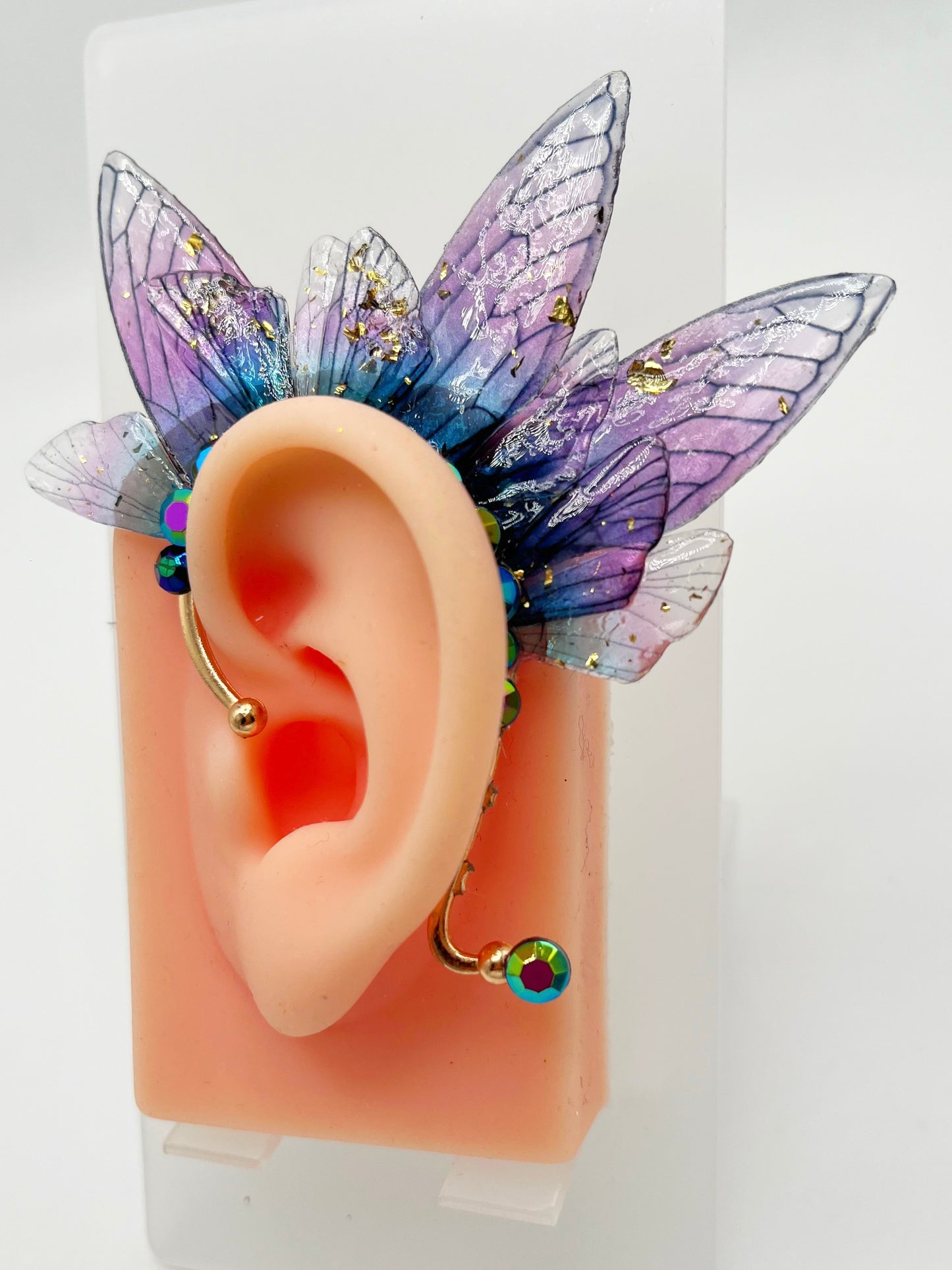 Purple fairy wing ear cuff with blue rhinestone, modeled on an ear.