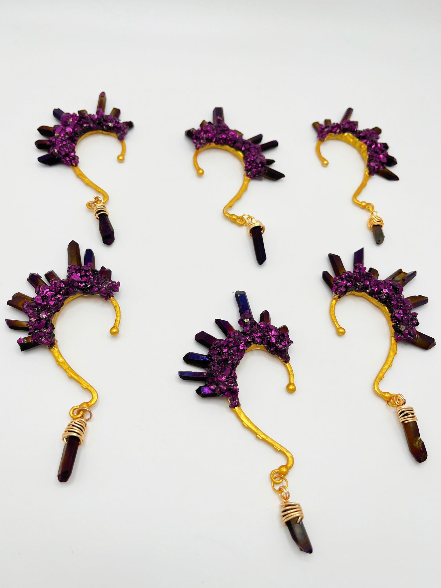 Six purple titanium coated quartz ear cuffs with a wire wrapped stone hanging from the bottom of each cuff. Each cuff is gold toned.