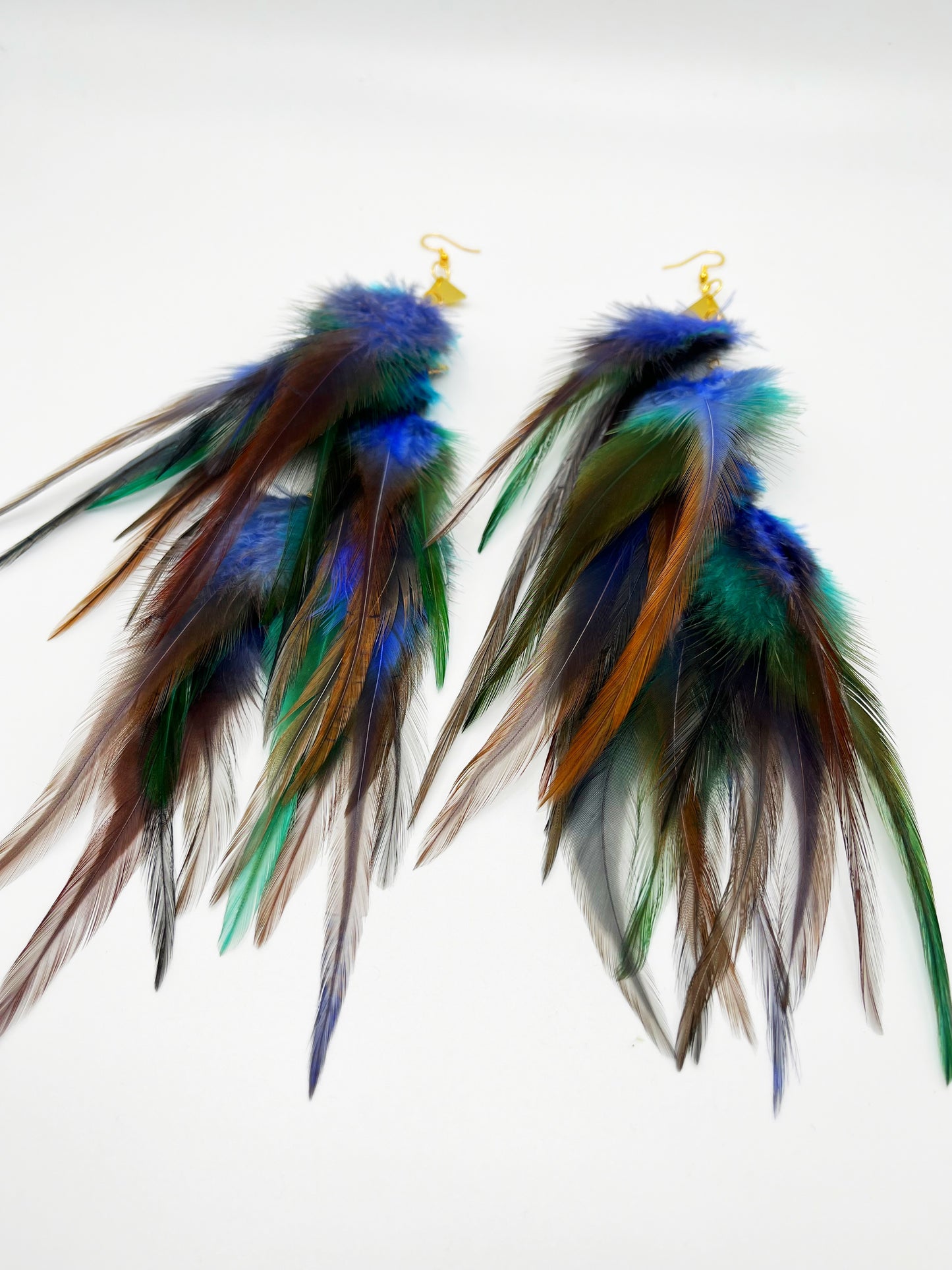Long bohemian feather earrings in blue, gray and turquoise tones, with gold triangle pendants.