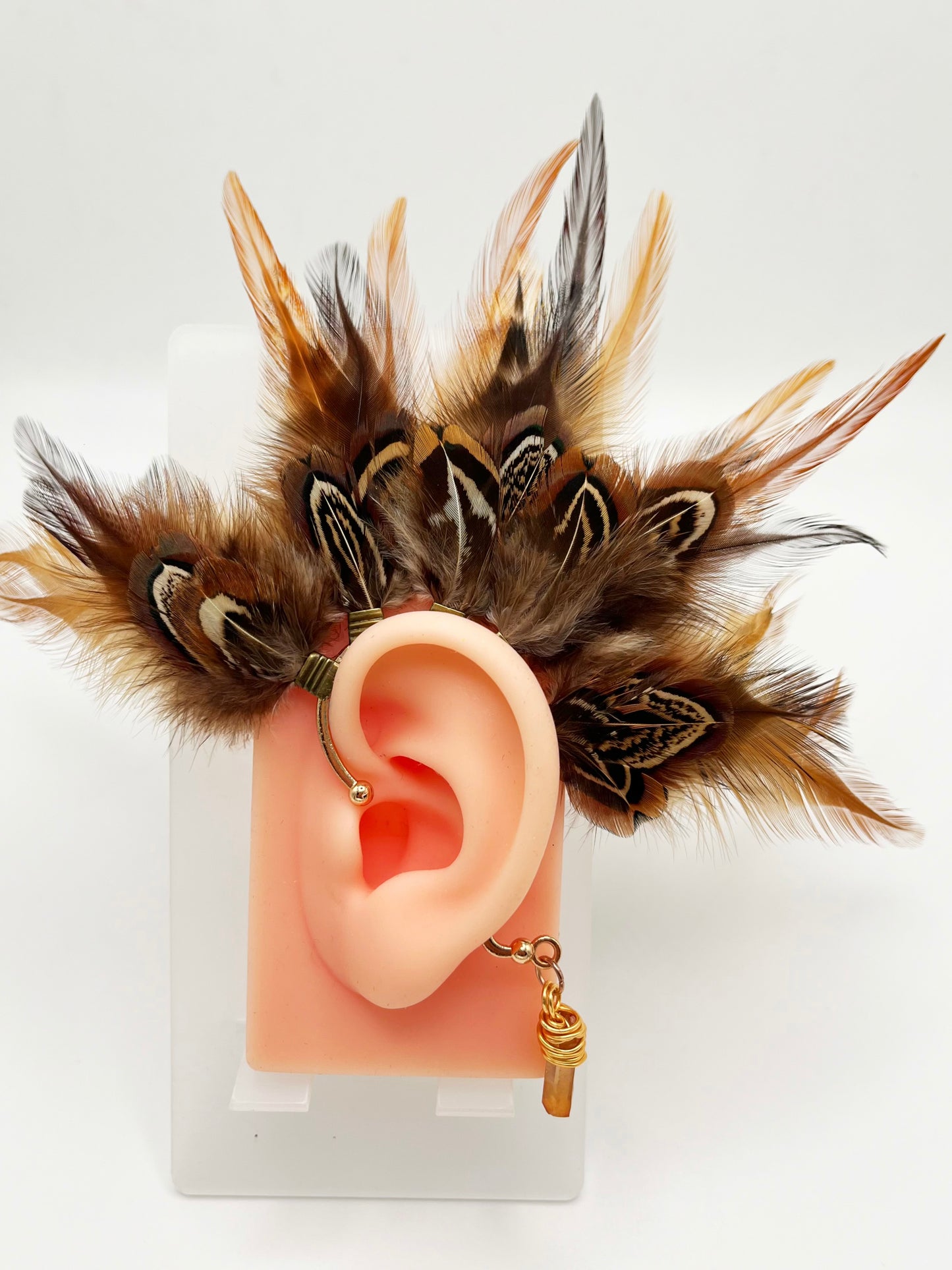 Rooster and pheasant feather ear cuff in brown and beige colors, modeled on an ear. A wire wrapped stone hangs from the bottom of the cuff behind the ear.