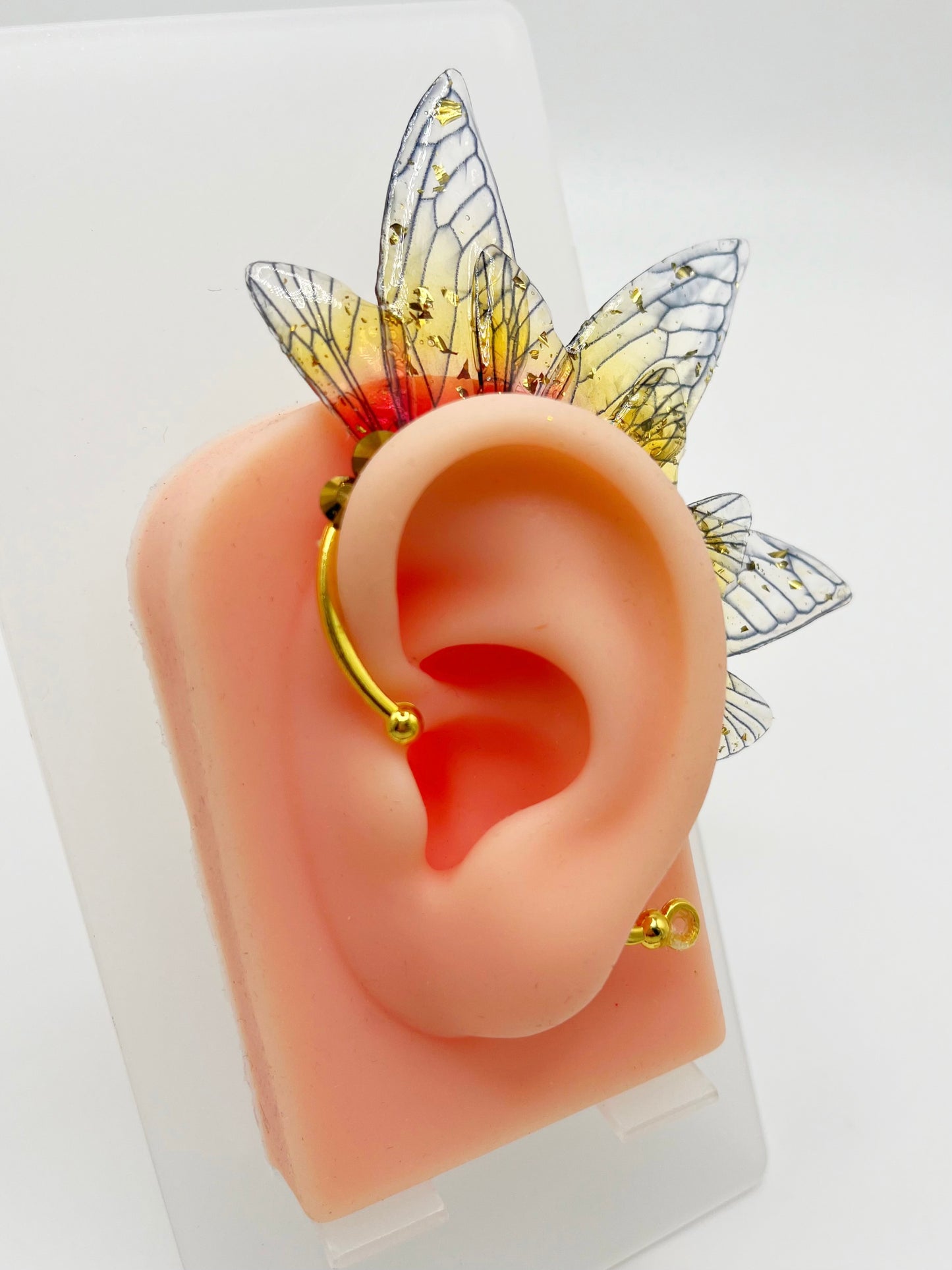 Yellow and red fairy wing ear cuff with gold rhinestones, modeled on an ear.
