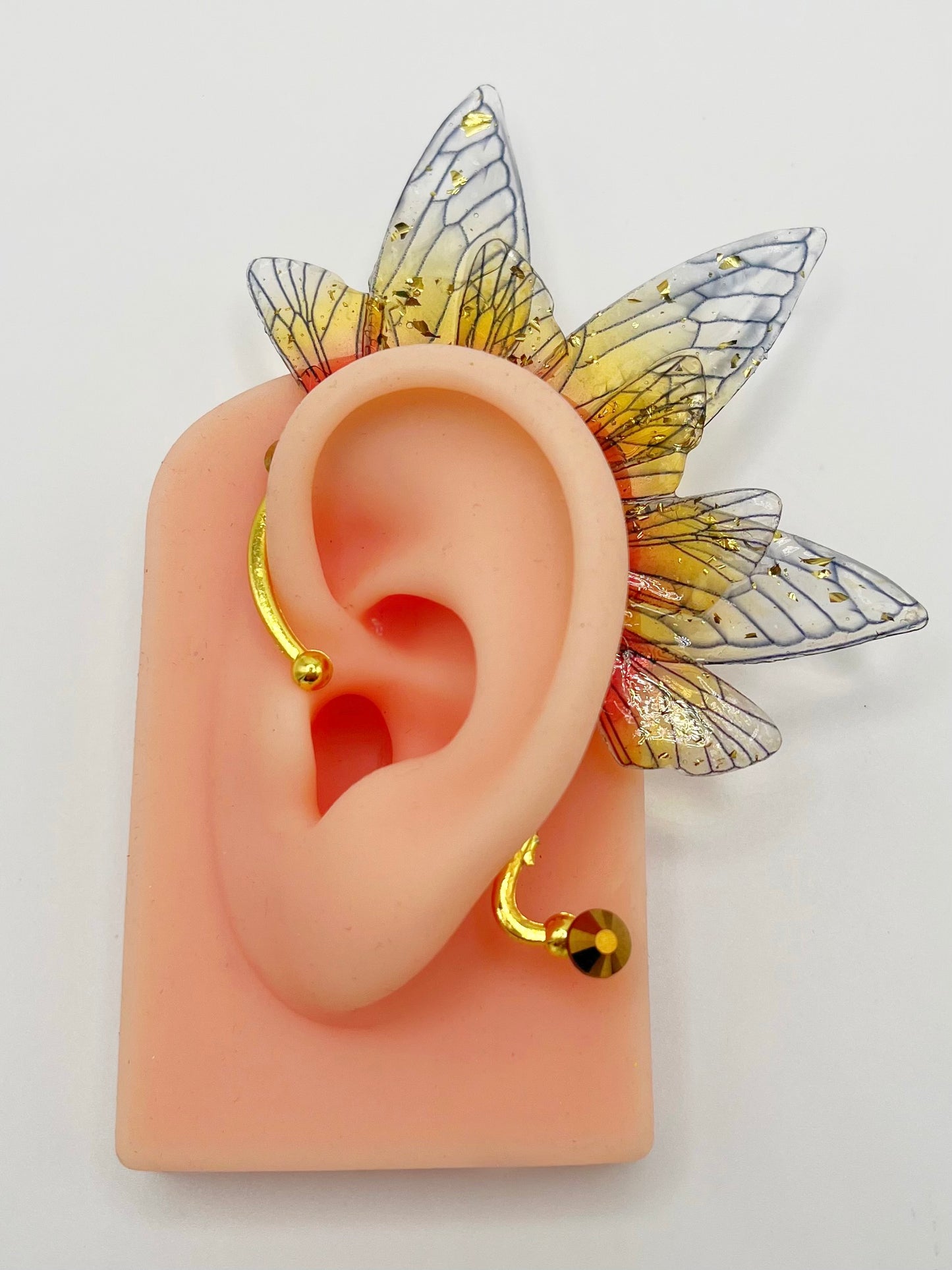 Yellow and red fairy wing ear cuff with gold rhinestones, modeled on an ear.