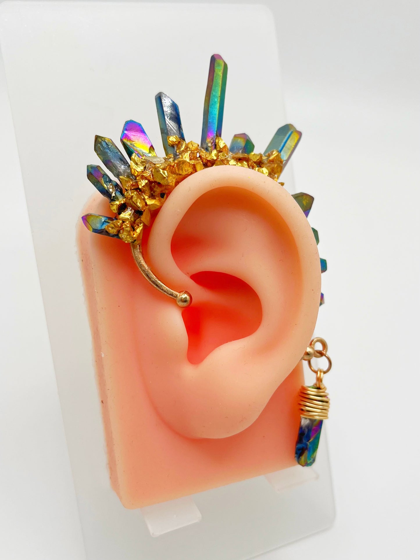 Blue rainbow titanium quartz crystal ear cuff with gold accents, modeled on an ear. A wire wrapped stone hangs from the bottom of the cuff behind the ear.