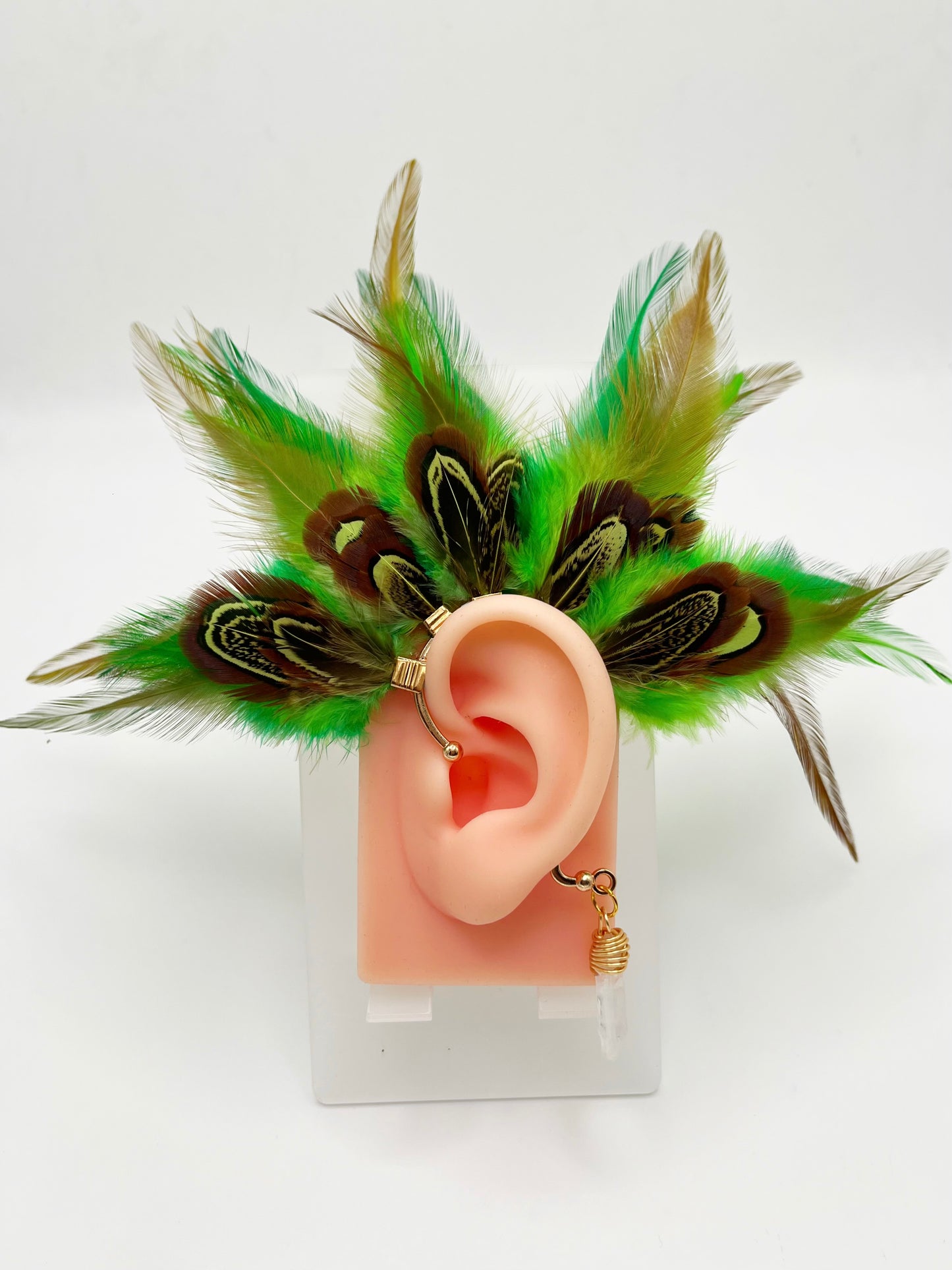 Vibrant green rooster feather ear cuff with brown green pheasant feathers, modeled on an ear. A wire wrapped quartz stone hangs from the cuff behind the ear.