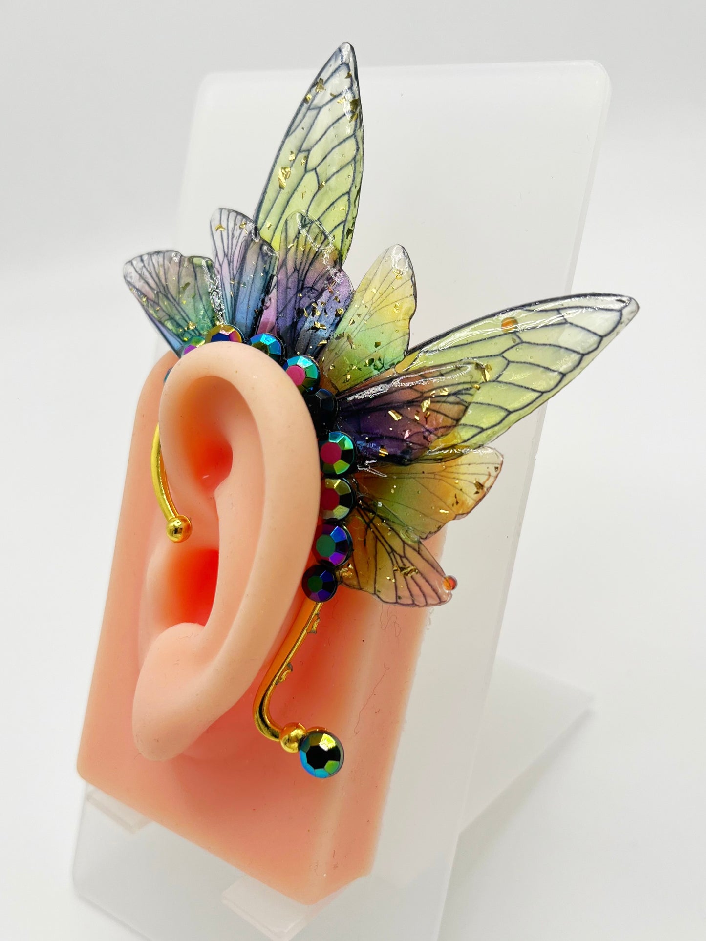 Green and purple fairy wing ear cuff with blue rhinestones, modeled on an ear.