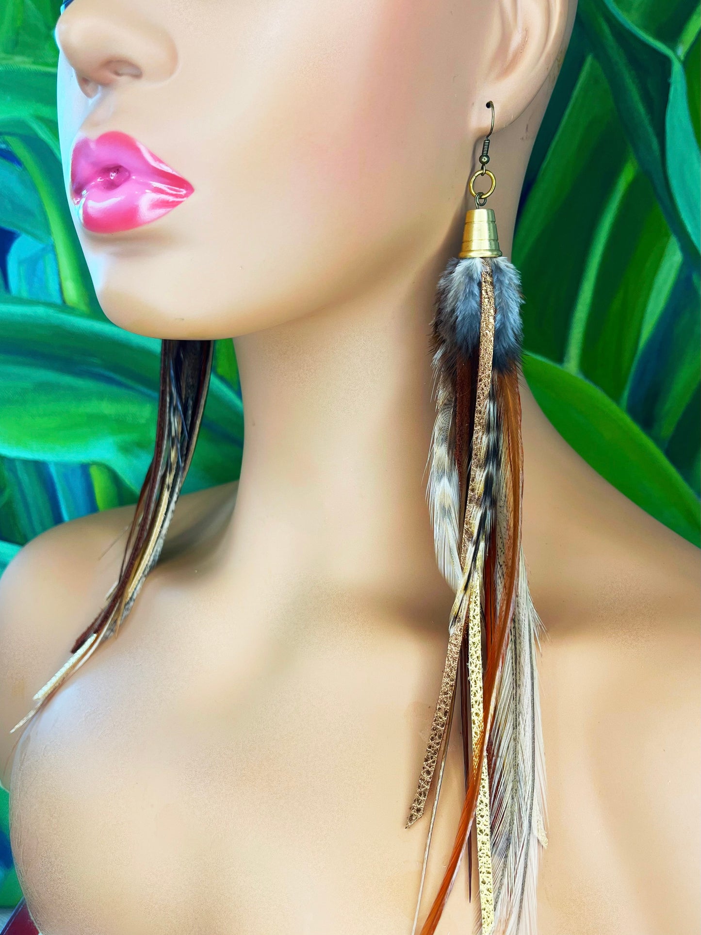 A model wearing dark brown feather earrings with metallic gold and bronze leather strips, hanging from a gold colored cap pendant.