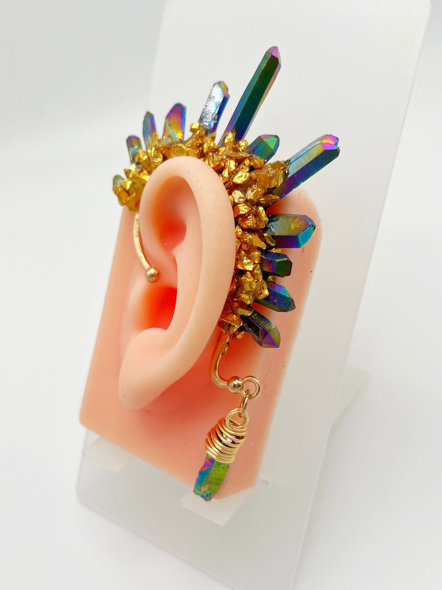 Blue rainbow titanium quartz crystal ear cuff with gold accents, modeled on an ear. A wire wrapped stone hangs from the bottom of the cuff behind the ear.