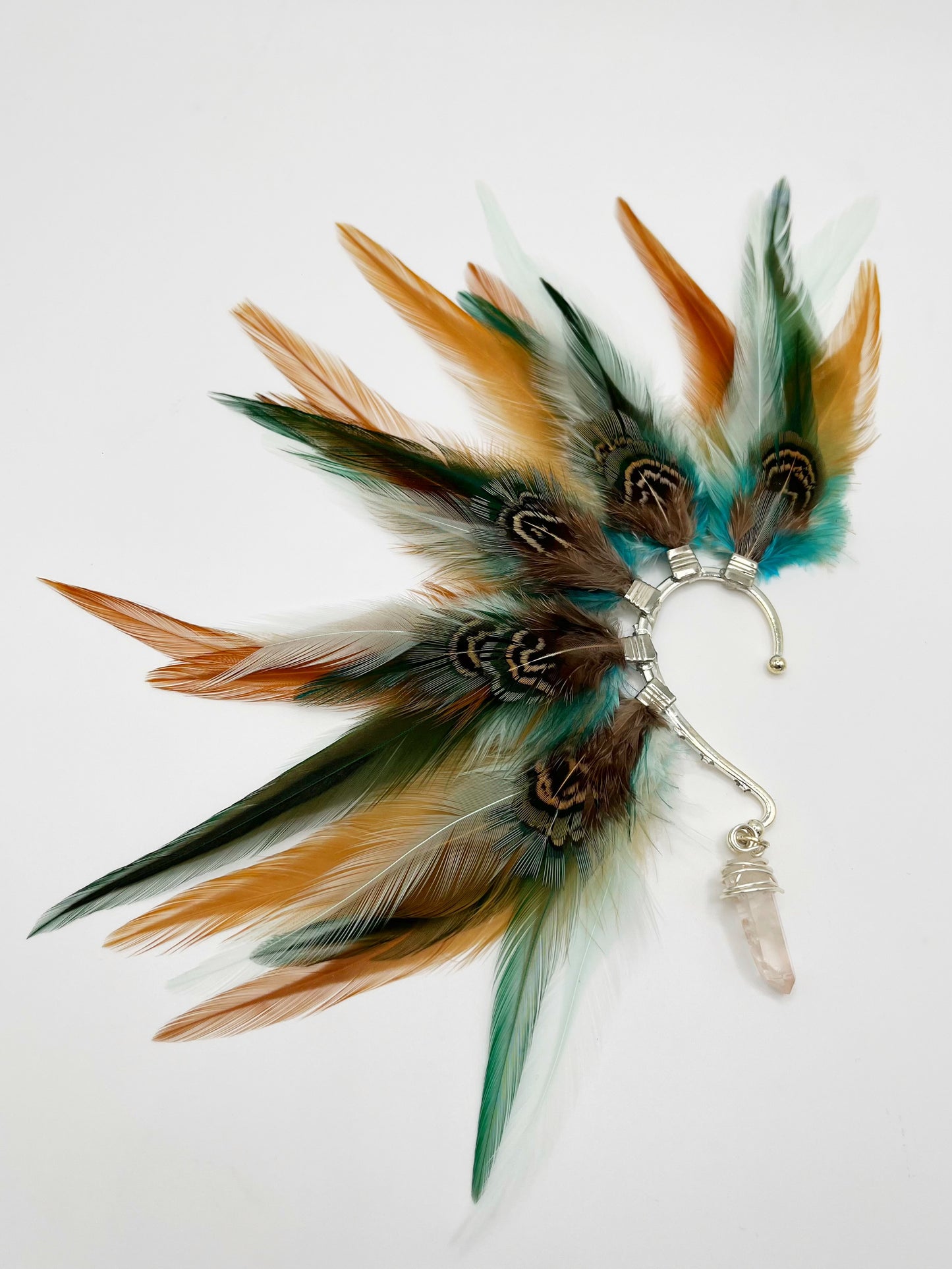 Rooster and pheasant feather ear cuff in green, turquoise and beige tones. A wire wrapped quartz stone hangs from the bottom of the cuff.