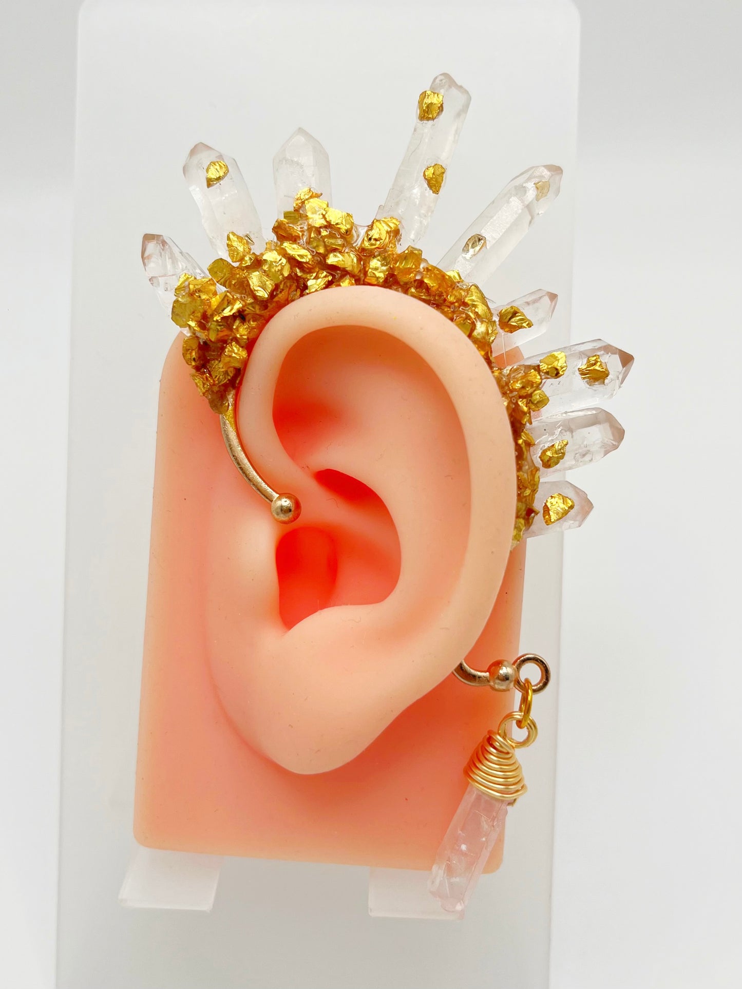 Clear quartz crystal ear cuff with crushed gold accents, modelled on an ear. A wire wrapped quartz stone hangs from the bottom of the cuff behind the ear.