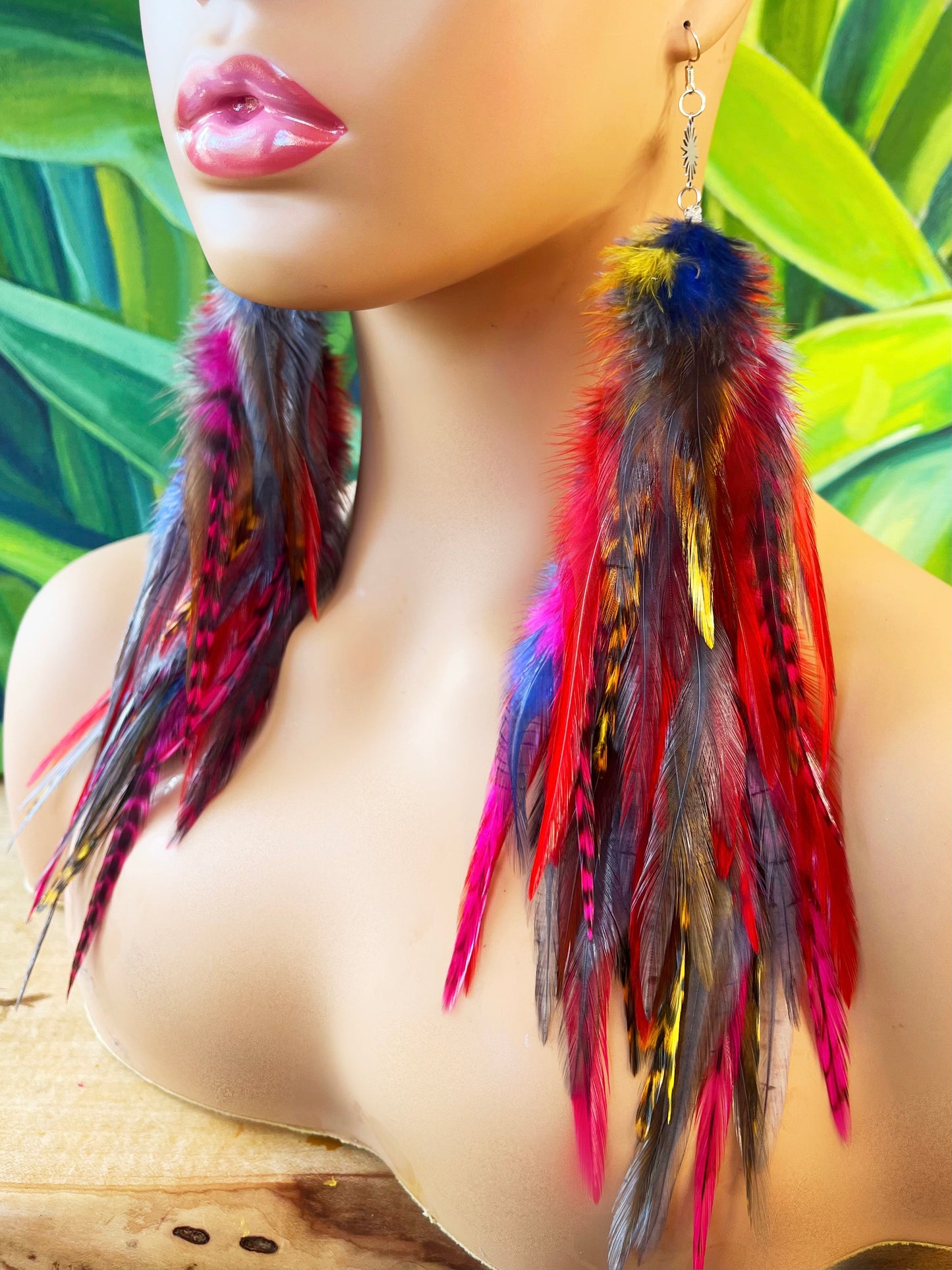 A mannequin head wearing long bohemian feather earrings, in cascading shades of gray, yellow, red, pink and blue.