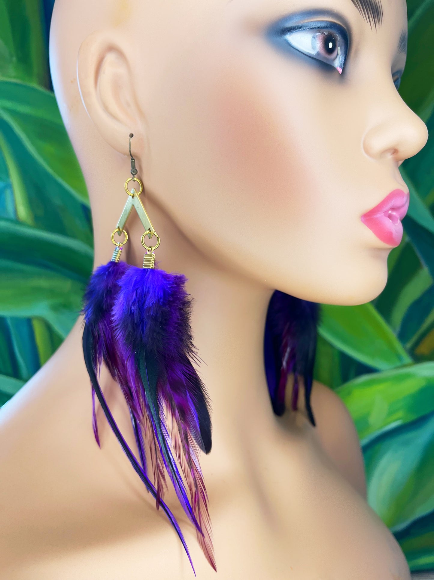A mannequin is wearing long feather earrings, in shades of purple and black. The feathers hang from a gold colored pendant of an arrow.