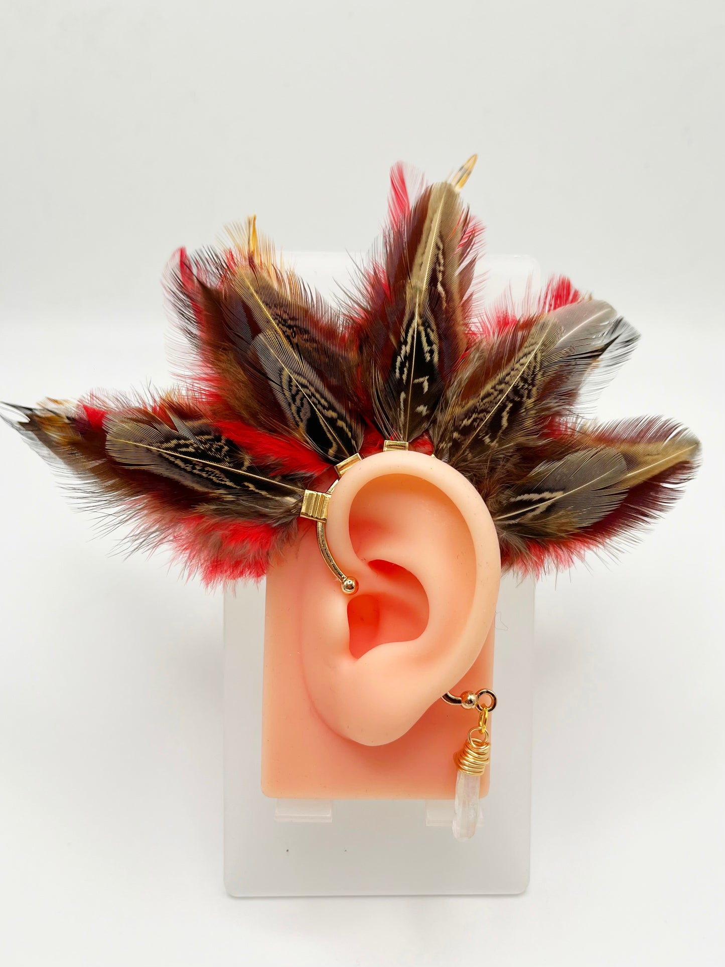 Brown pheasant and vibrant red rooster feather ear cuff, modeled on an ear. A wire wrapped quartz crystal hangs from the cuff behind the ear.