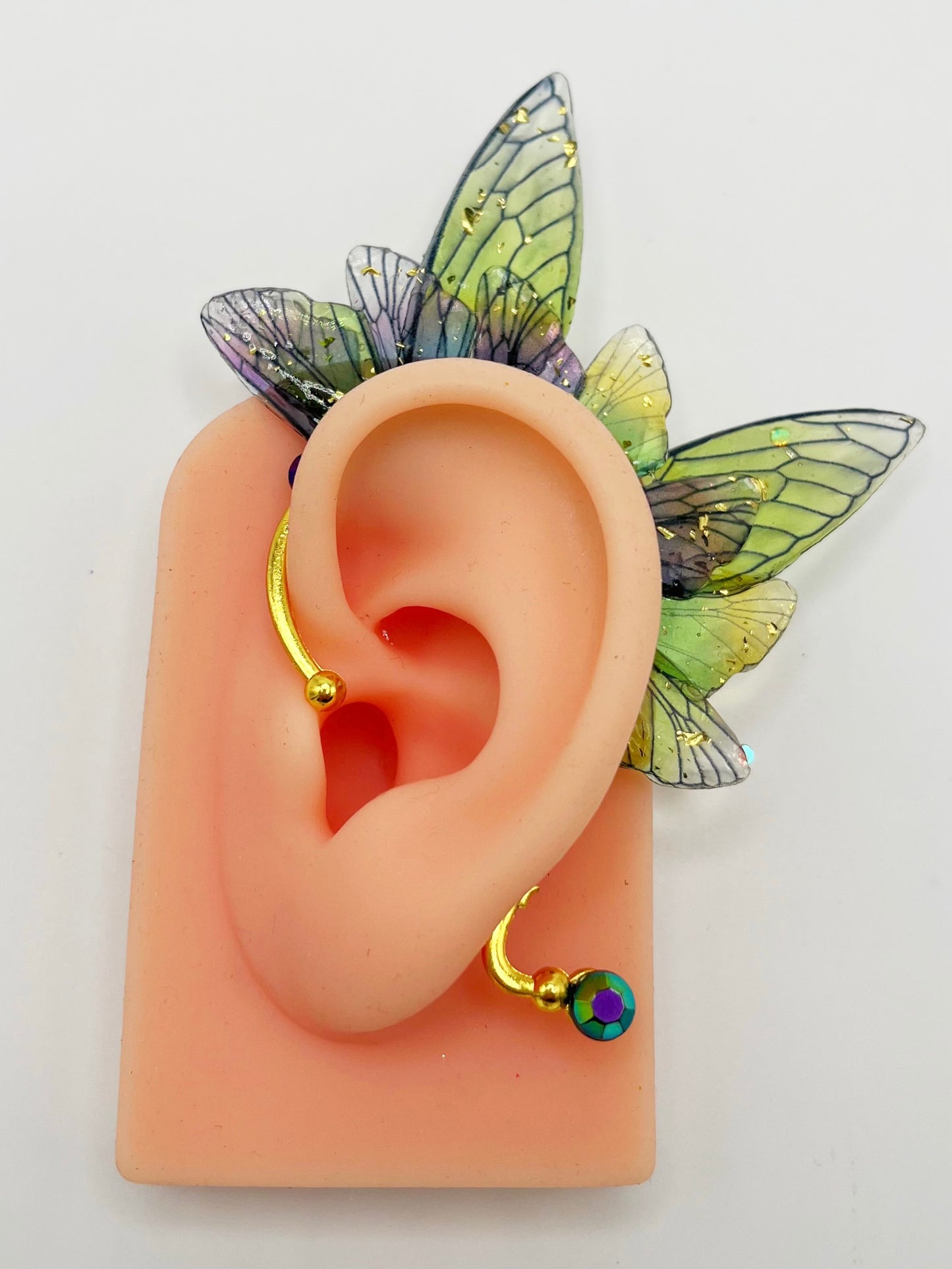 Green and purple fairy wing ear cuff with blue rhinestones, modeled on an ear.