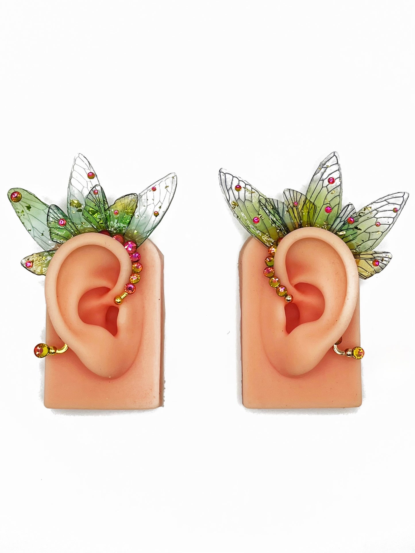 A pair of green fairy wing ear cuffs with pink rhinestones, modeled on a pair of ears.
