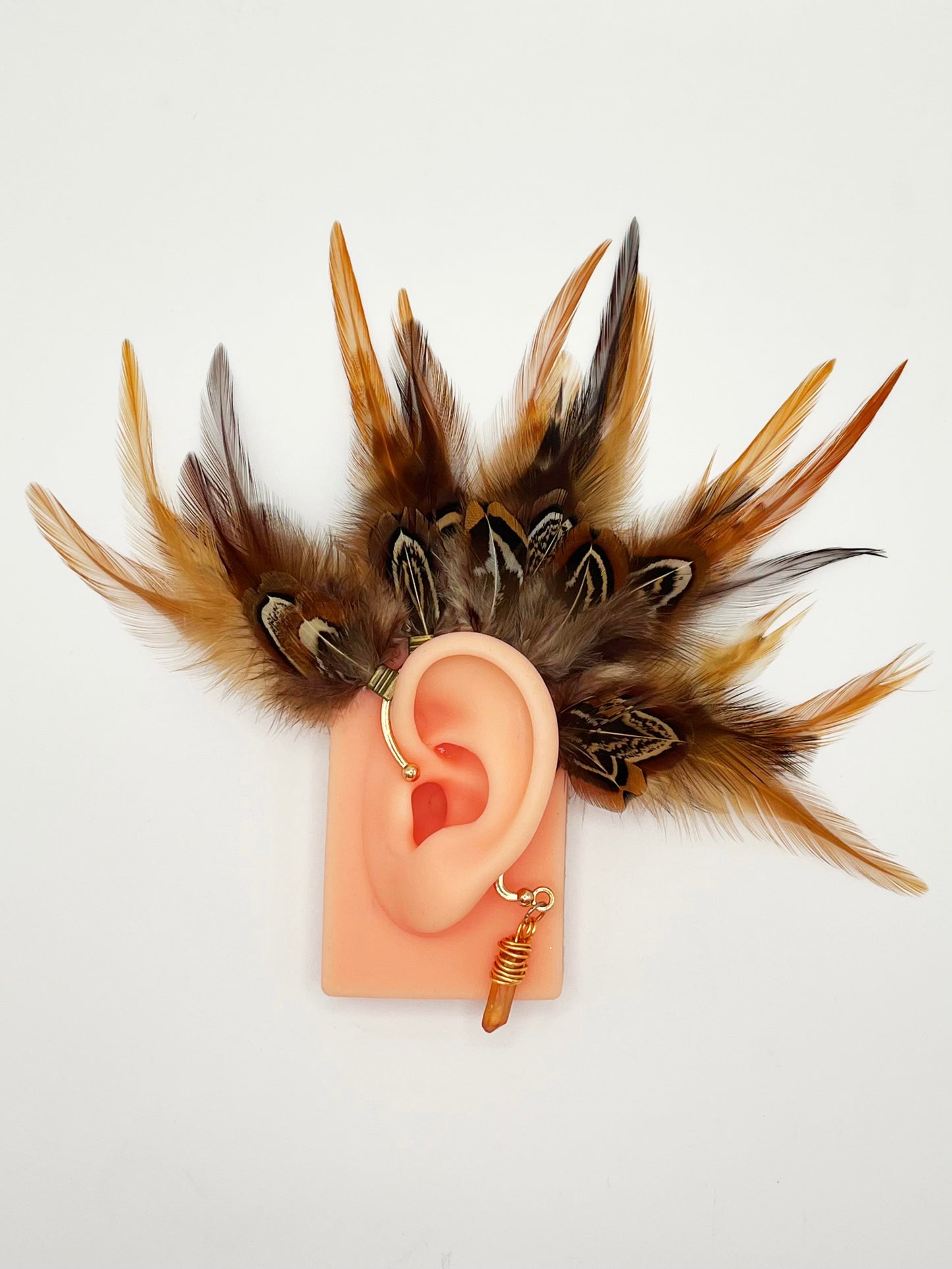 Rooster and pheasant feather ear cuff in brown and beige colors, modeled on an ear. A wire wrapped stone hangs from the bottom of the cuff behind the ear.