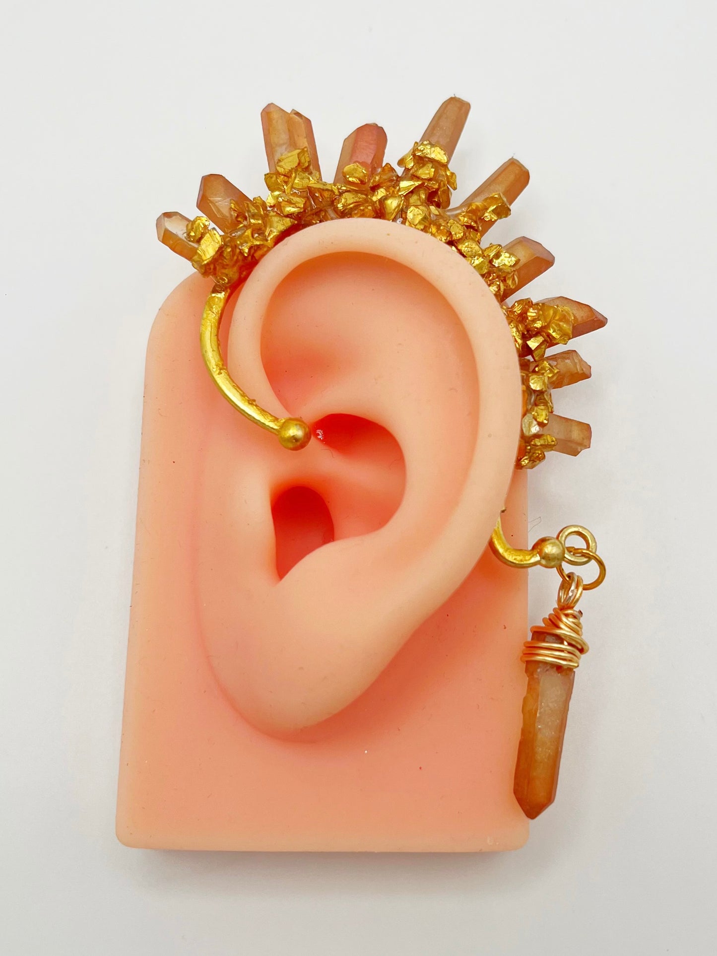 Orange citrine crystal ear cuff with crushed gold accents, modeled on an ear. A wire wrapped stone hangs from the bottom of the cuff behind the ear.