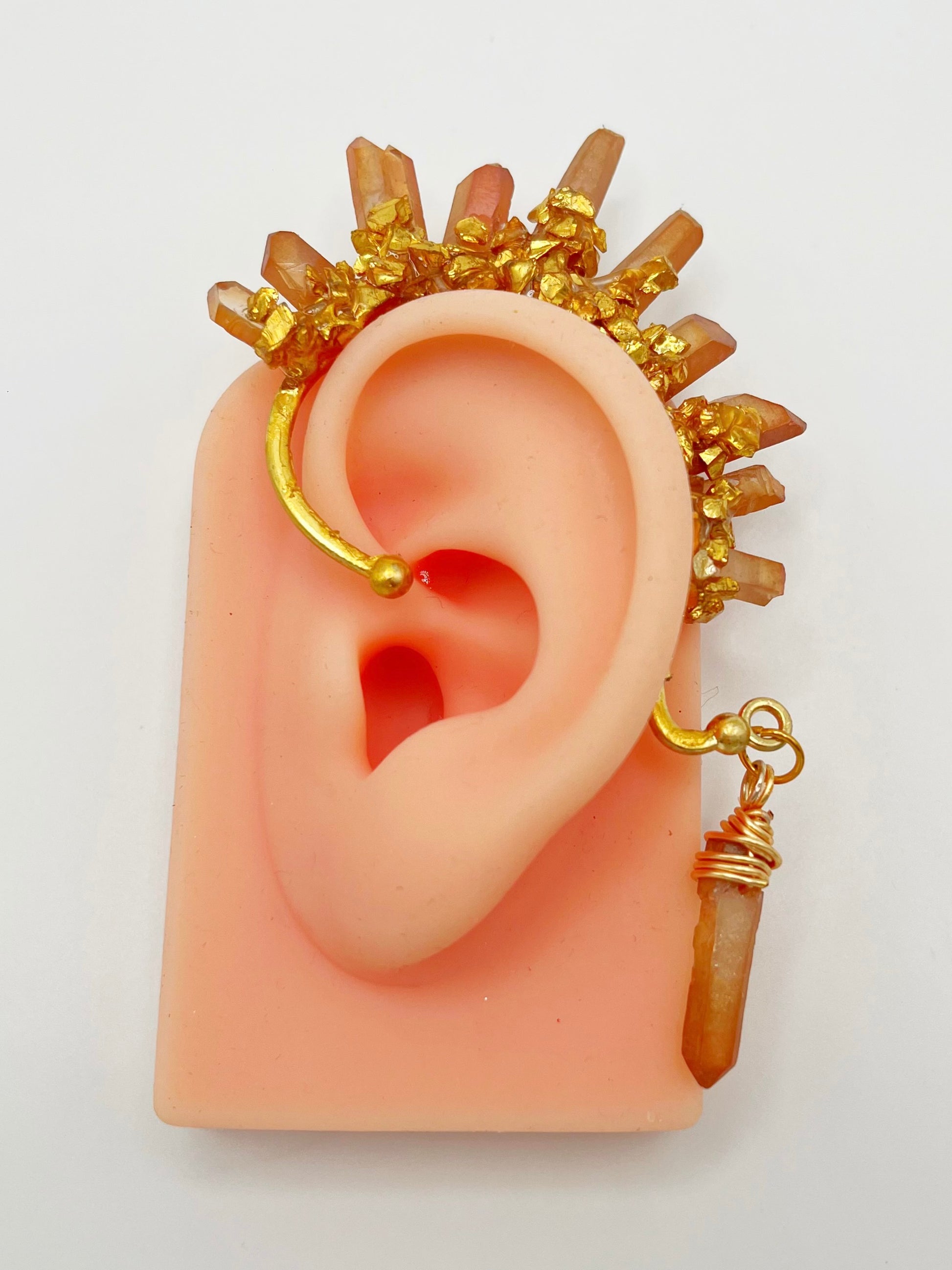 Orange citrine crystal ear cuff with crushed gold accents, modeled on an ear. A wire wrapped stone hangs from the bottom of the cuff behind the ear.