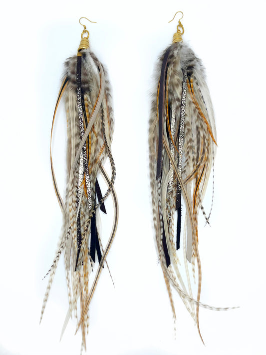 Long thick feather earrings in natural tones, with hand cut leather strips. All feather and leather hangs from underneath a gold cap pendant. 