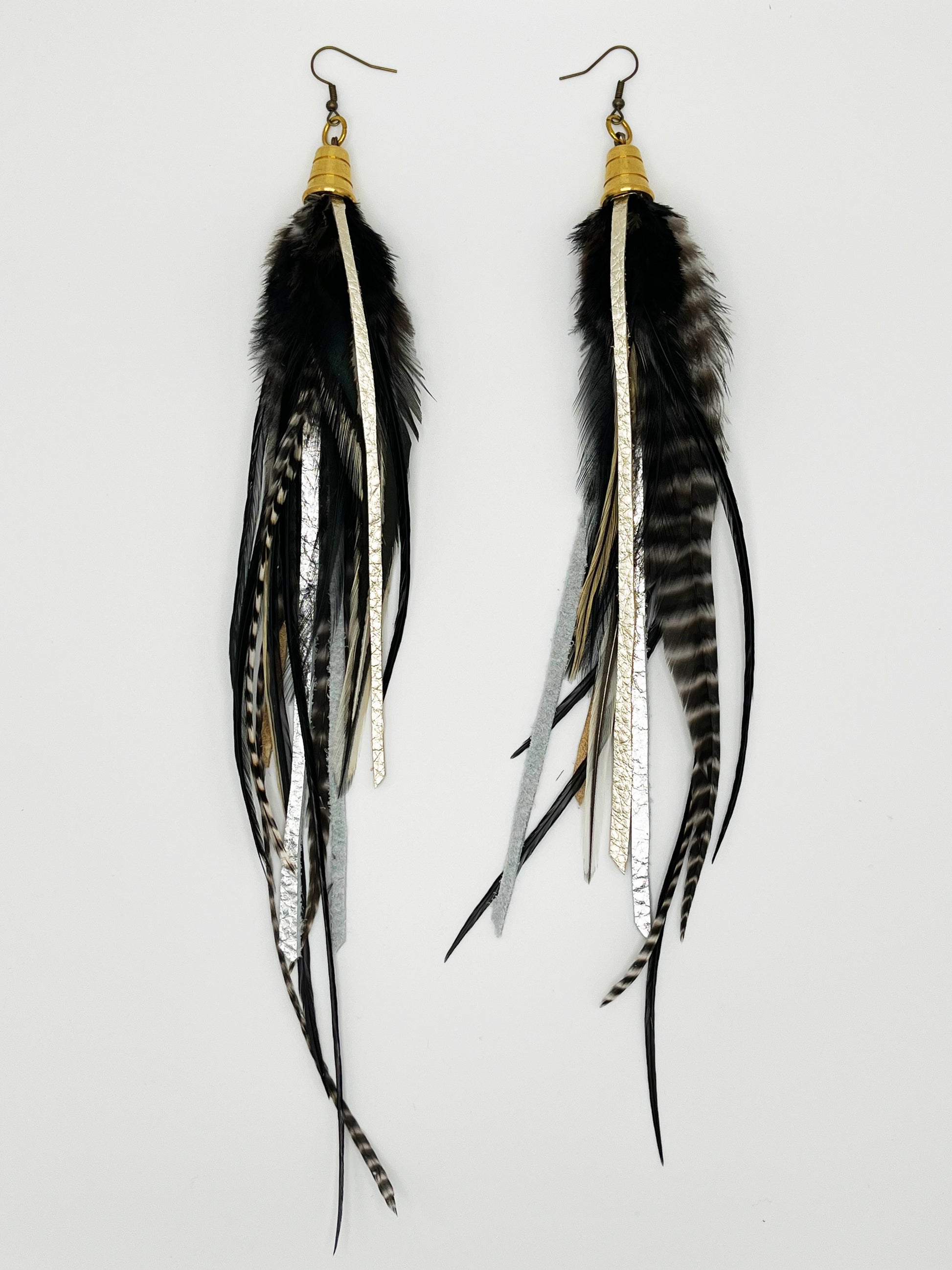 Long black and white feather earrings, with metallic pewter colored leather strips, hanging from a gold colored cap pendant.