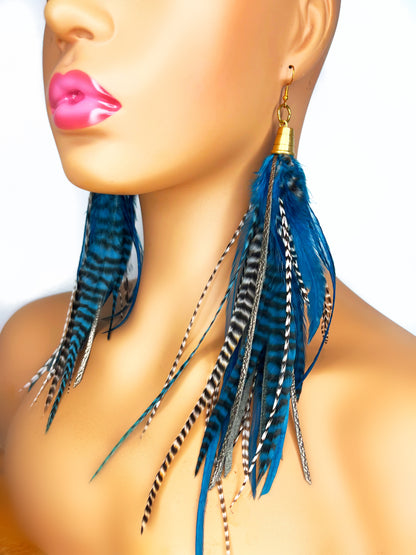 Mannequin wearing long teal rooster feather earrings with strips of metallic bronze leather. Feathers and leather hang from under a gold colored pendant.