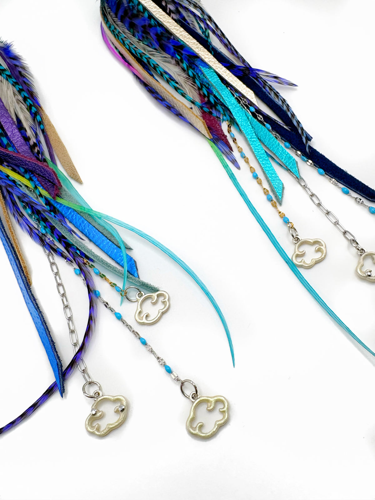 A pair of bohemian-style feather and leather tassels with silver cloud-shaped charms, shown on a clean white background.