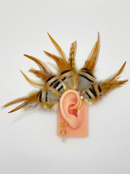 Rooster and chukar partridge feather ear cuff in white, cream, yellow and beige tones, modeled on an ear. A wire wrapped quartz stone dangles from the cuff behind the ear.