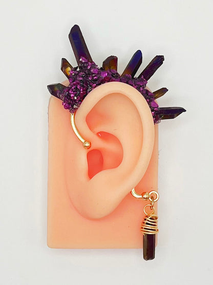 Purple titanium quartz ear cuff with purple metallic accents, modeled on an ear. A wire wrapped quartz hangs from the bottom of the cuff behind the ear.