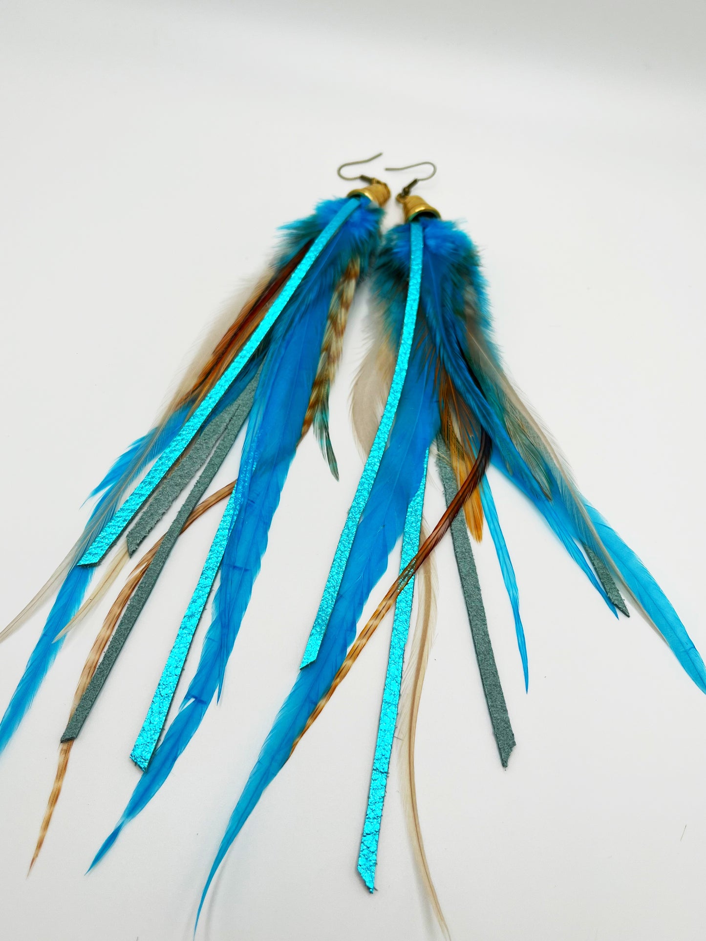 Long turquoise blue feather earrings with strips of metallic leather, hanging from a gold colored cap pendant.