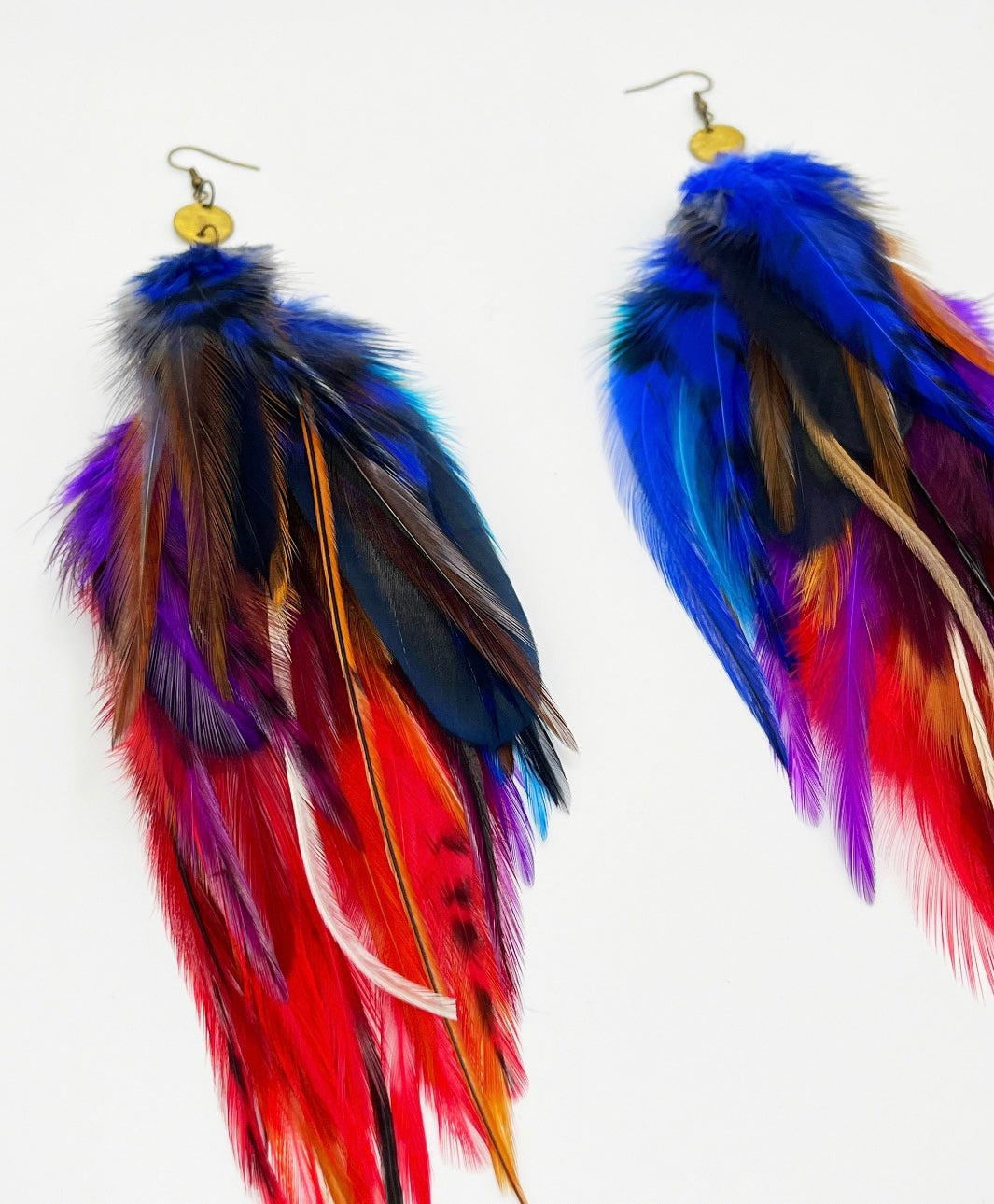  A pair of handcrafted long feather earrings with vibrant hues of red, blue, yellow, and purple, featuring a gold-colored bronze circular pendant and hypoallergenic ear wire, perfect for bohemian and festival-inspired fashion.