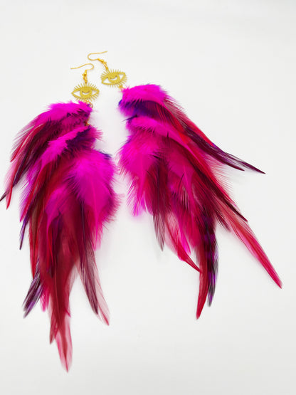 Long bohemian feather earrings in bright pink colors, hanging from a gold eye pendant. 